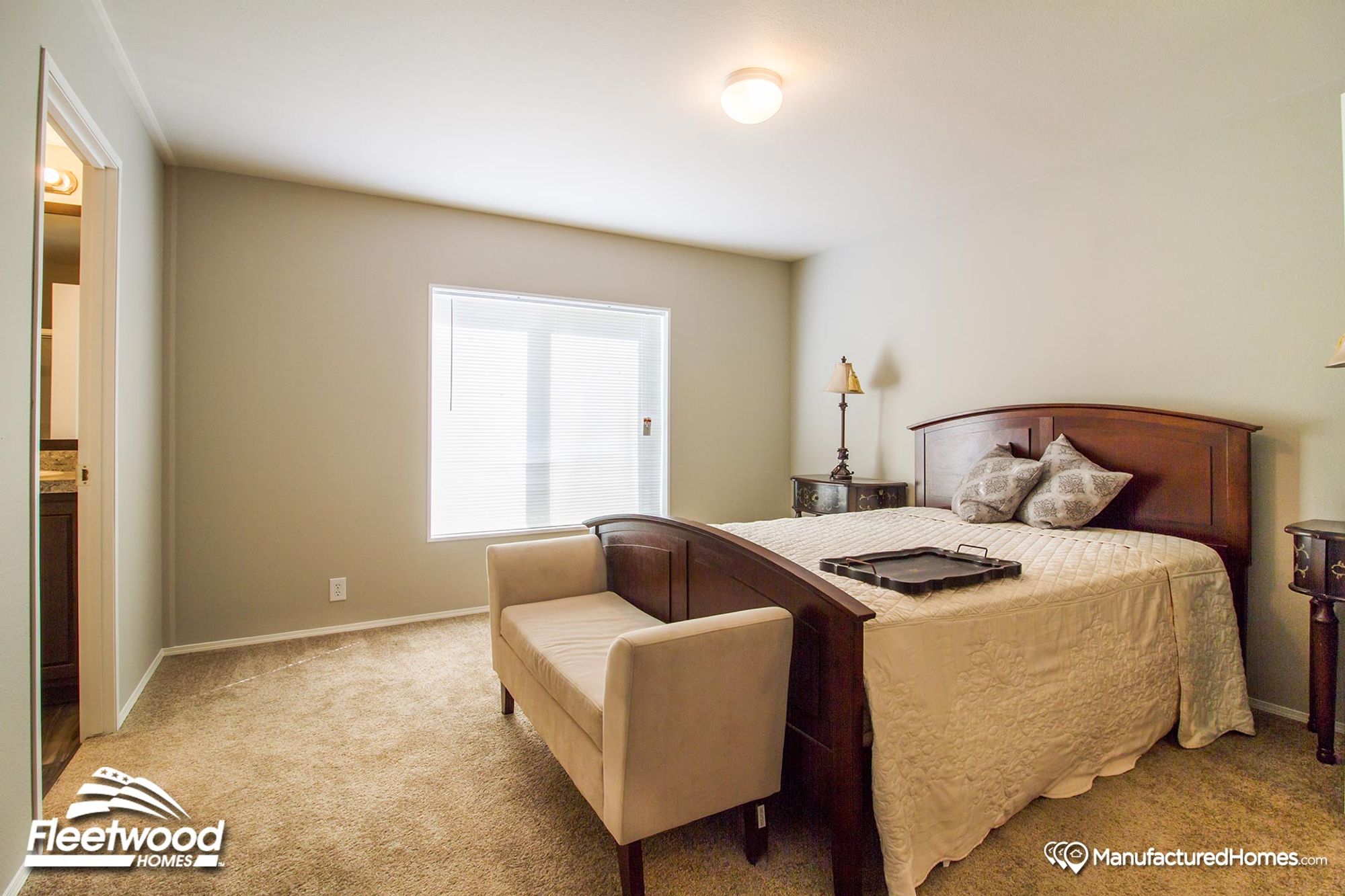 Bright bedroom with neutral tones, featuring a dark wood bed frame, cream quilted bedding, an upholstered bench at the foot of the bed, and vintage-style nightstands.