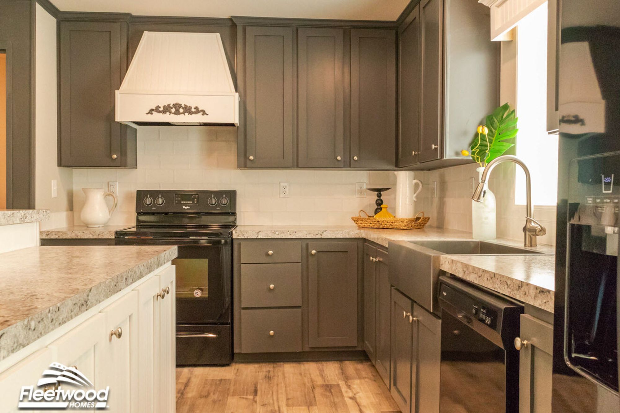 Warm kitchen with granite-style countertops, dark cabinetry, white range hood, black appliances, and a breakfast bar with white candle decor.