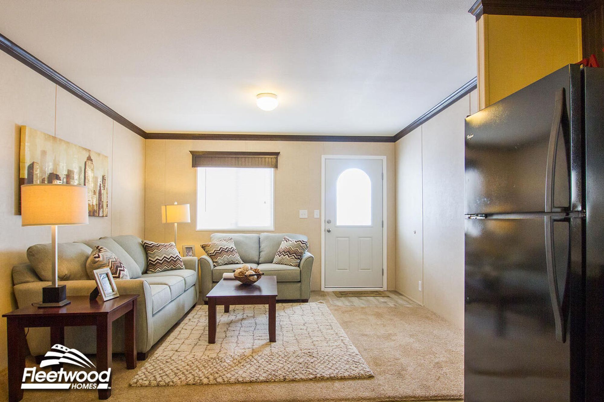 Cozy living room with beige walls, sofa set, coffee table, lamps, and window by the front door.