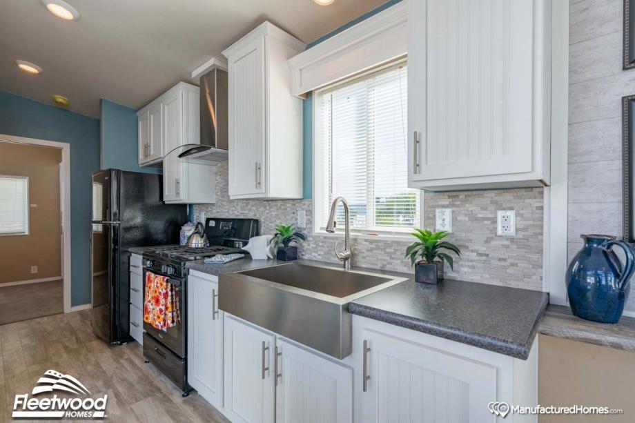 Bright kitchen with white shaker cabinets, gray stone backsplash, large stainless steel farmhouse sink, black Whirlpool appliances, and a window above the sink letting in natural light.