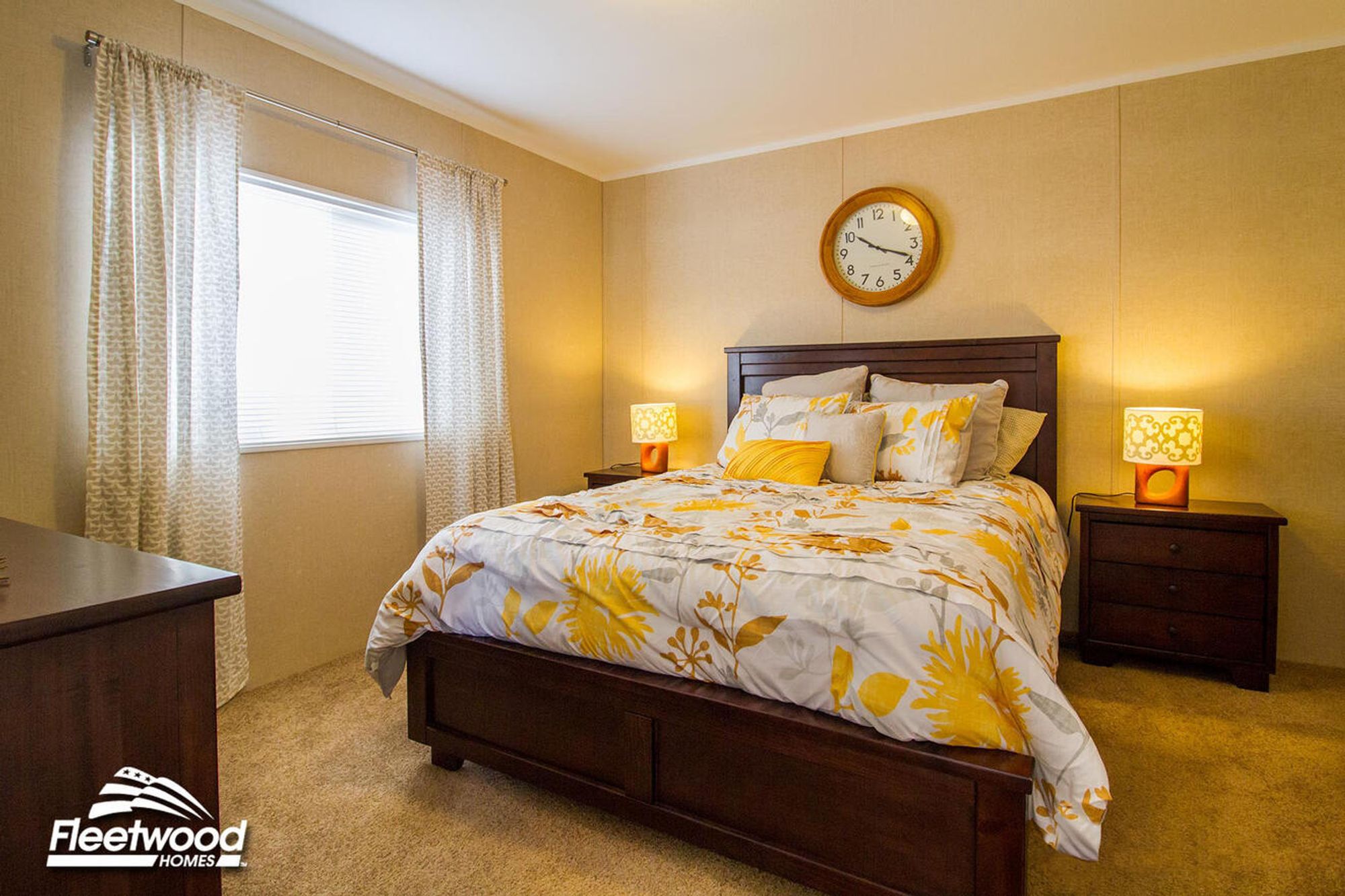 Bedroom with floral bedding, dresser with mirror, and window with light curtains.