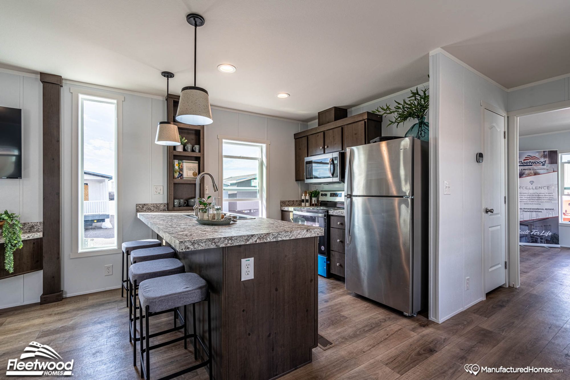 Modern kitchen with a marbled island featuring a stainless steel sink and three barstools, pendant lighting, dark wood cabinetry, and stainless steel appliances.
