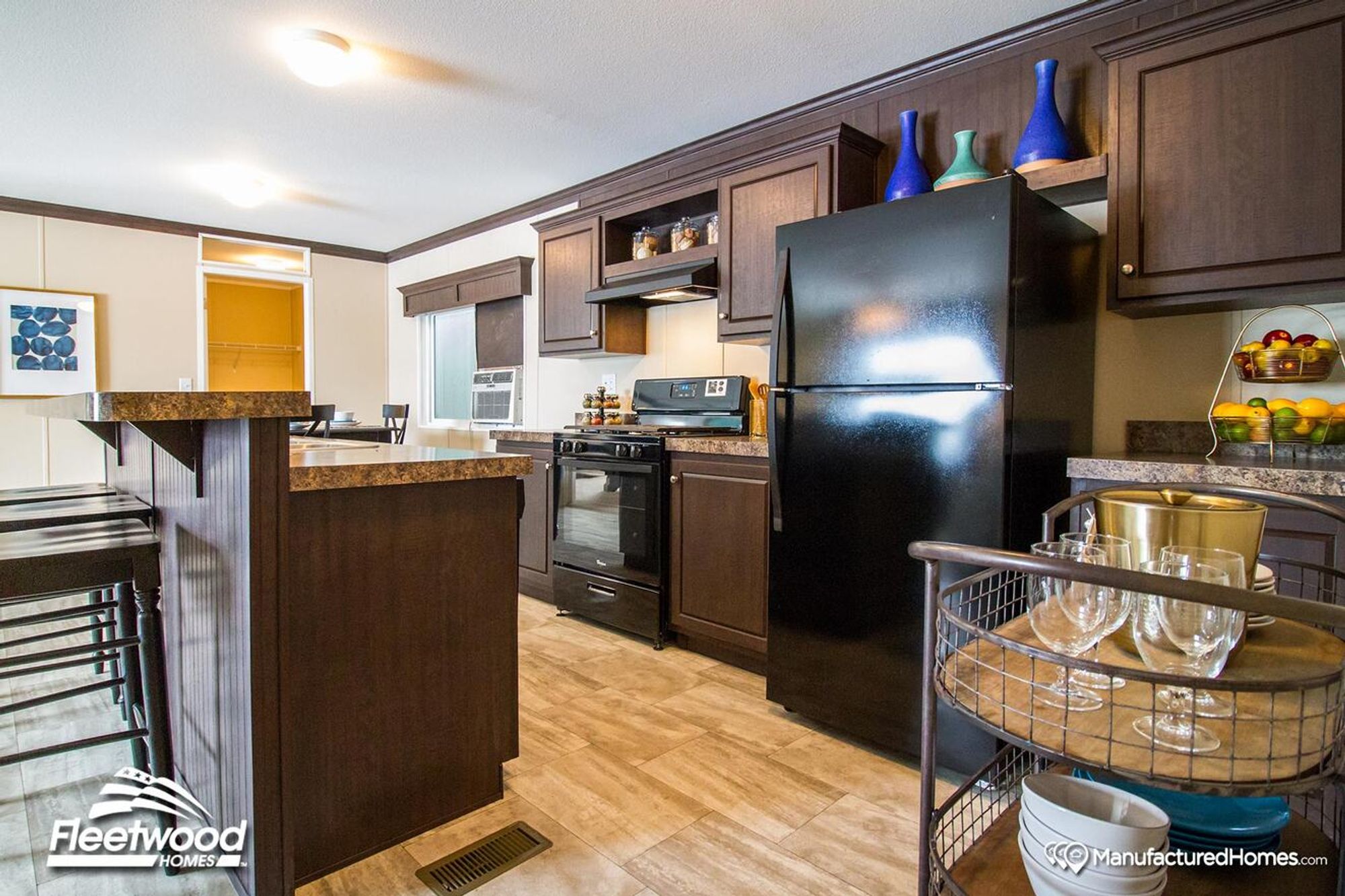 Kitchen with dark wood cabinets, black appliances, island bar seating, and rolling cart with glassware.