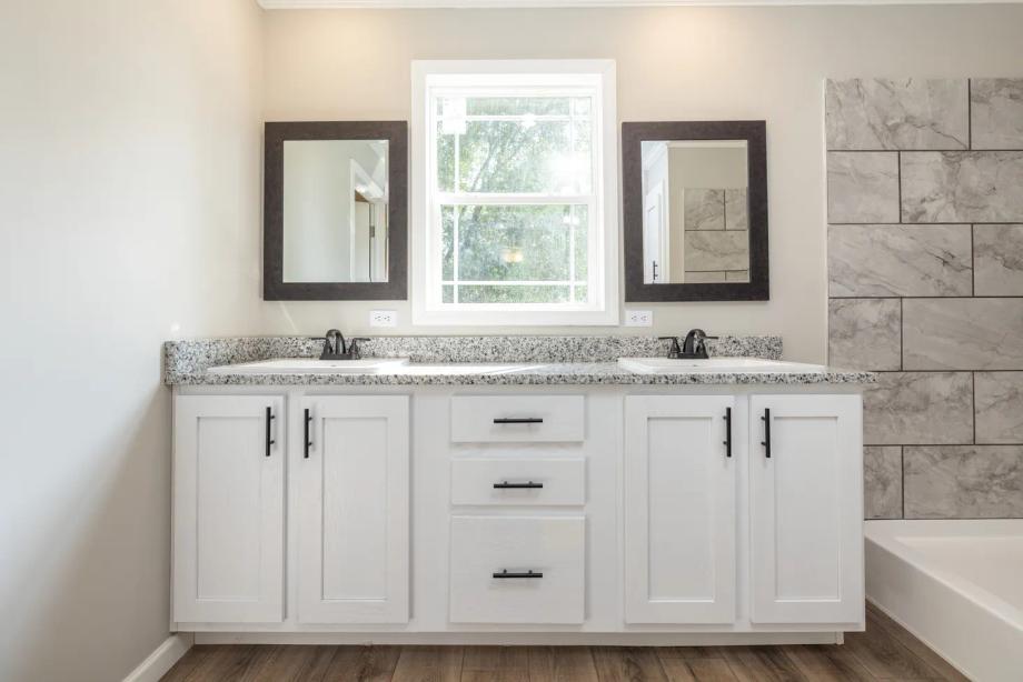 Double sinks with black-and-white speckled countertops, white cabinets, and marble-textured shower tiles