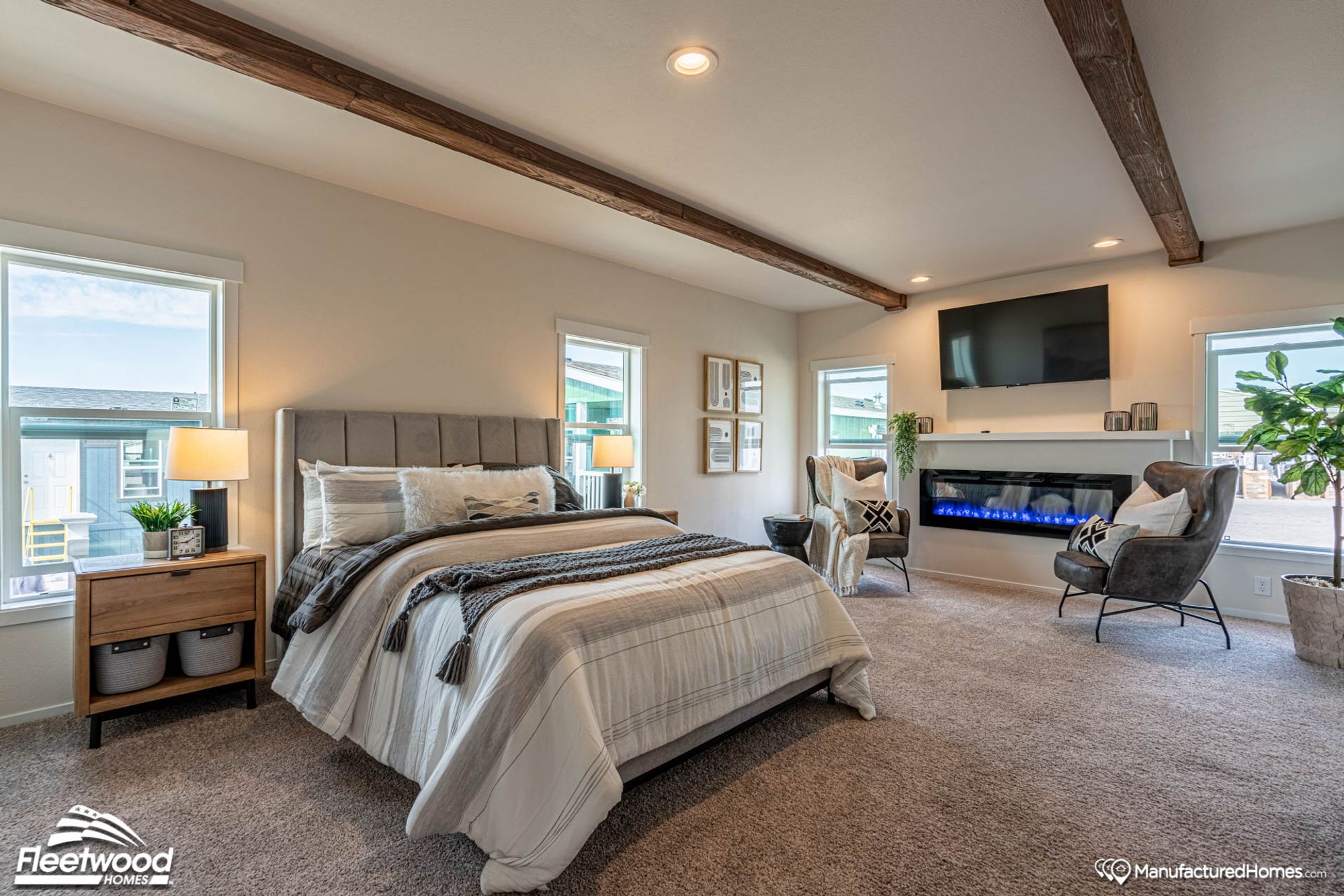 Large bedroom with two chairs, a large bed, and a fire place.