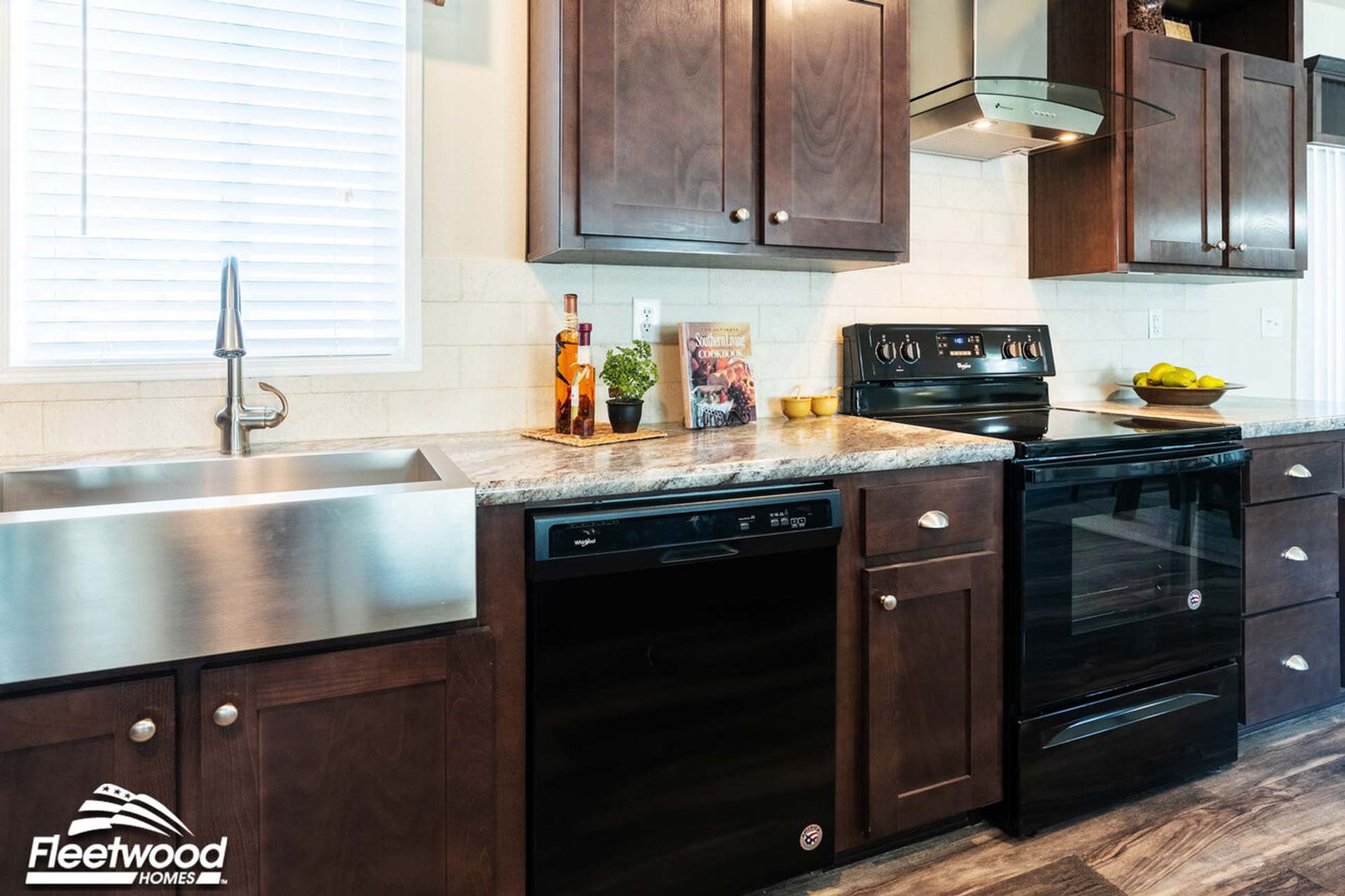 Kitchen with dark wood cabinets, stainless steel farmhouse sink, black dishwasher and oven, granite countertops, and modern range hood.