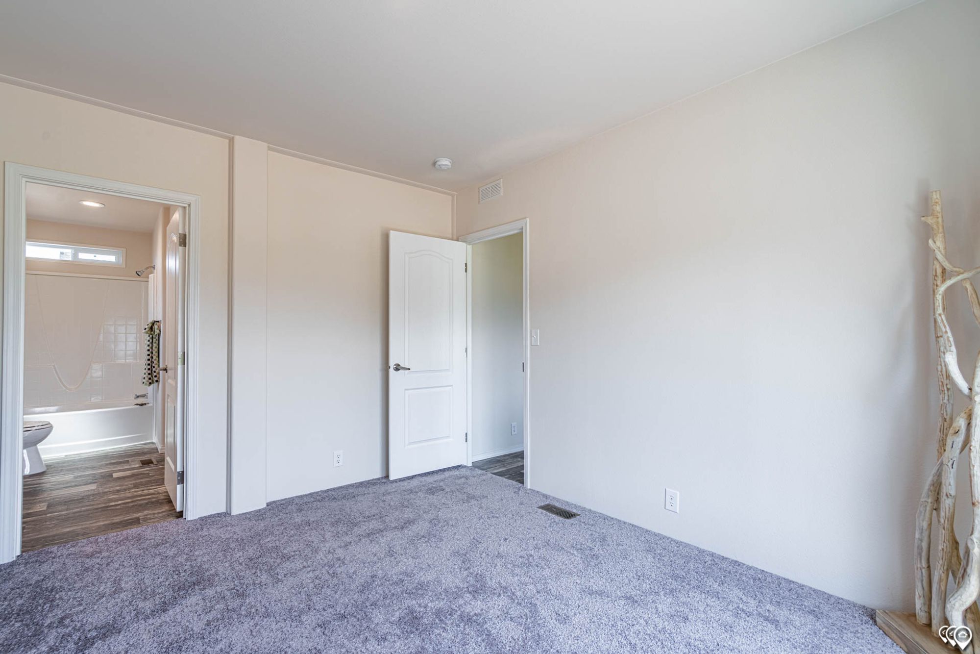 Empty bedroom with a partial view into a mid-sized bathroom.