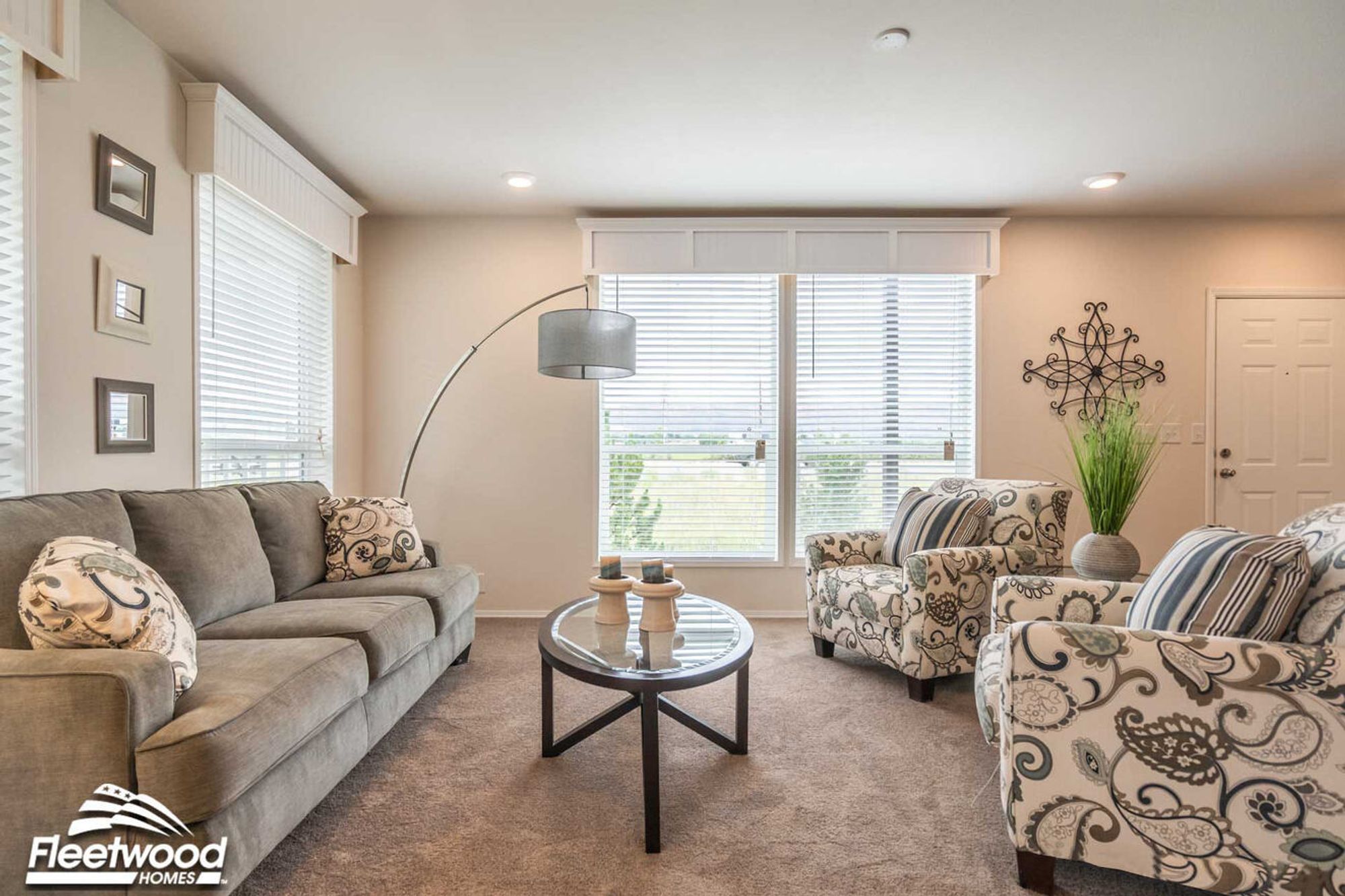 Open living space with patterned armchairs, glass coffee table, and view into a modern kitchen with bar seating and dining area.