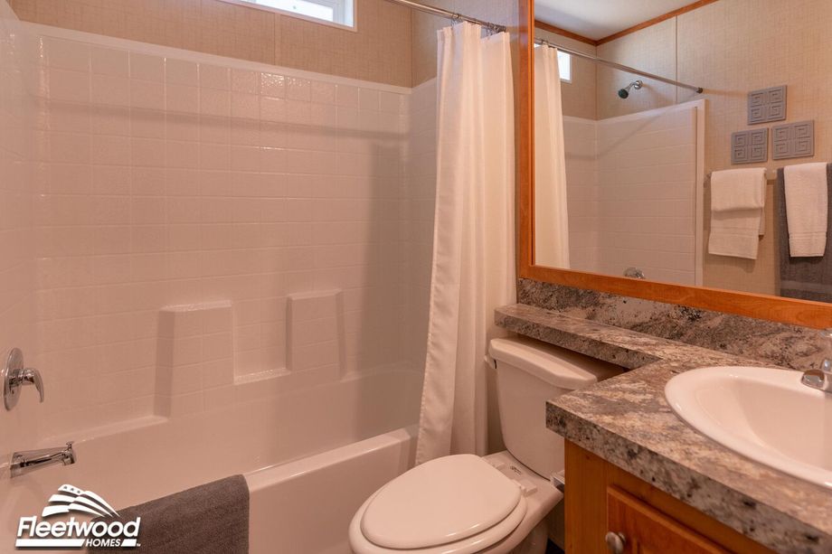 Bathroom with a white tiled shower and tub combo, granite countertop vanity, and a large framed mirror.
