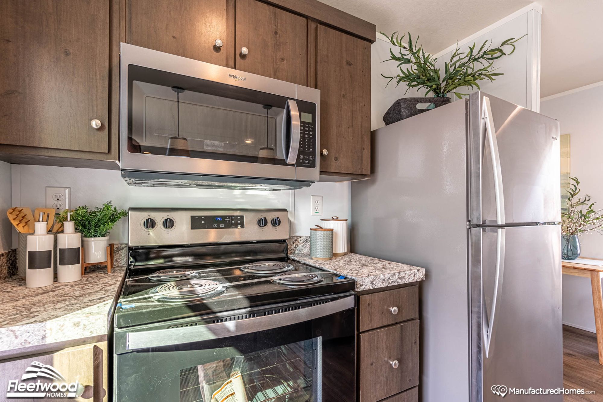 Compact kitchen with stainless steel Whirlpool appliances, including a microwave, electric stove, and refrigerator, set against dark wood cabinetry and marbled countertops.