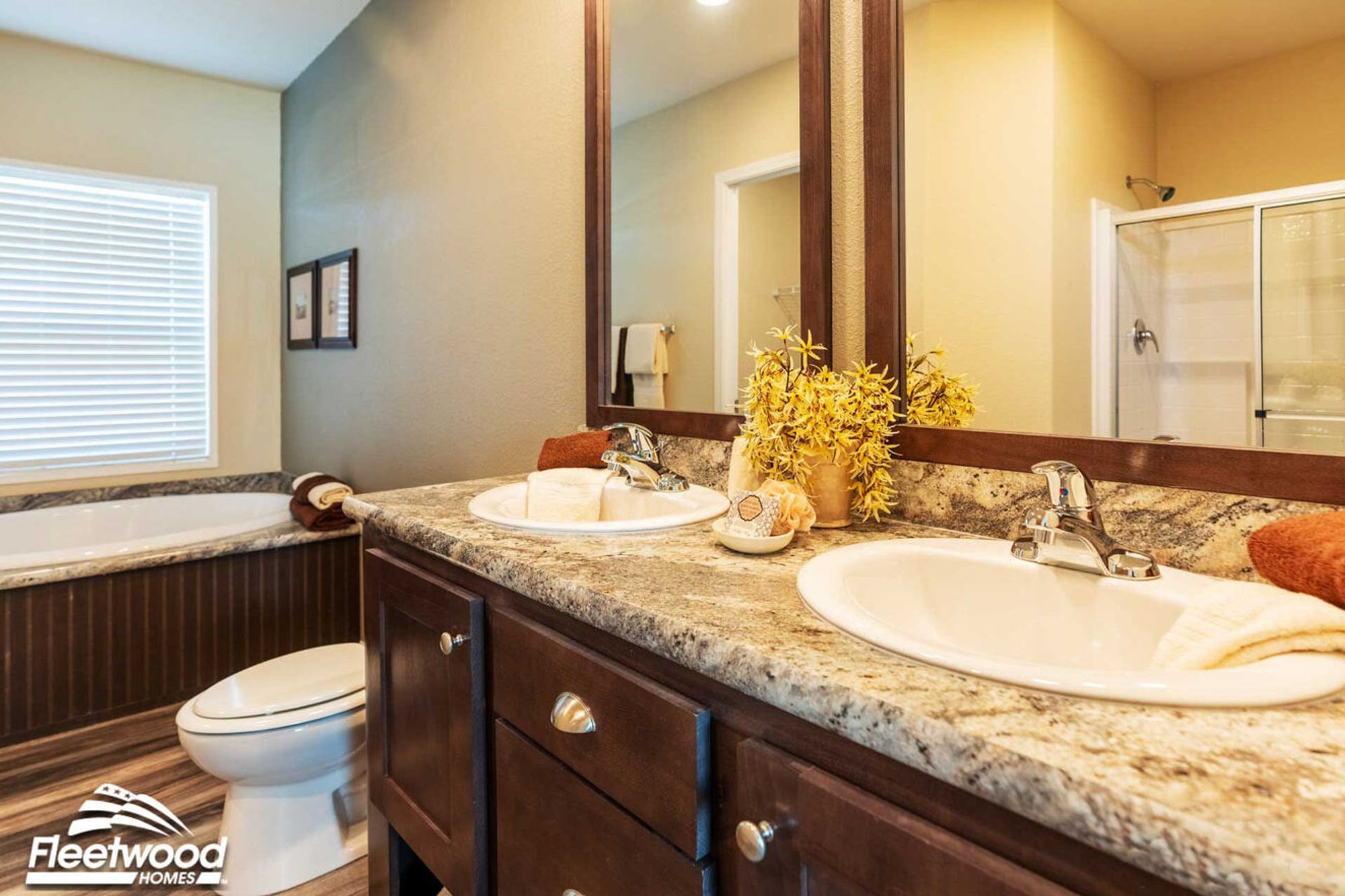 Bathroom with dual sinks, granite countertops, large mirror, soaking tub, and glass-enclosed shower.