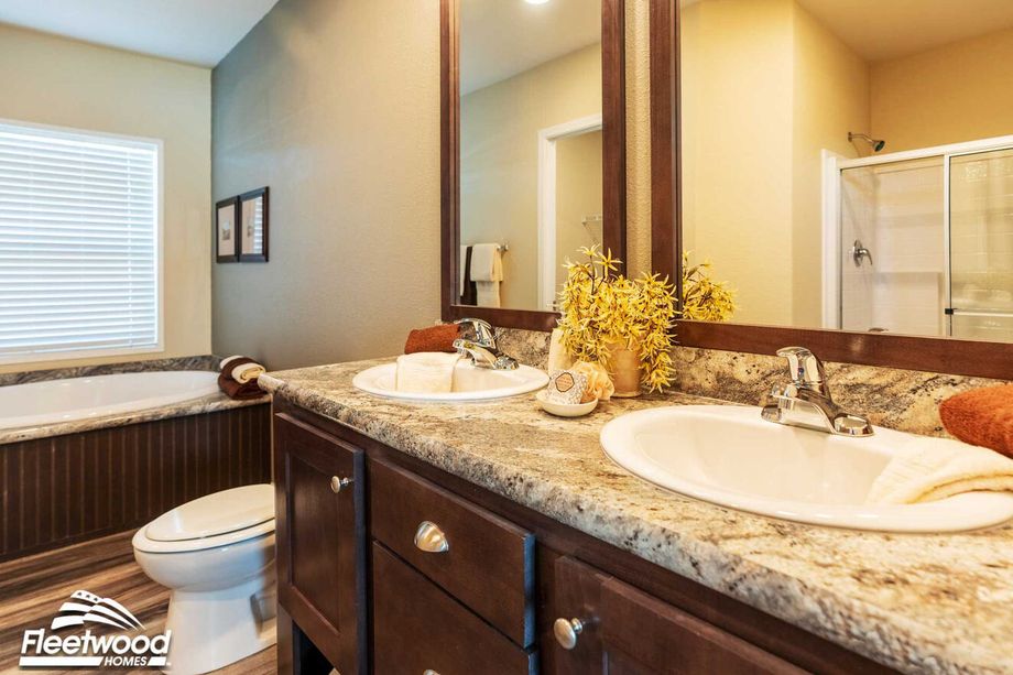 Bathroom with dual sinks, granite countertops, large mirror, soaking tub, and glass-enclosed shower.