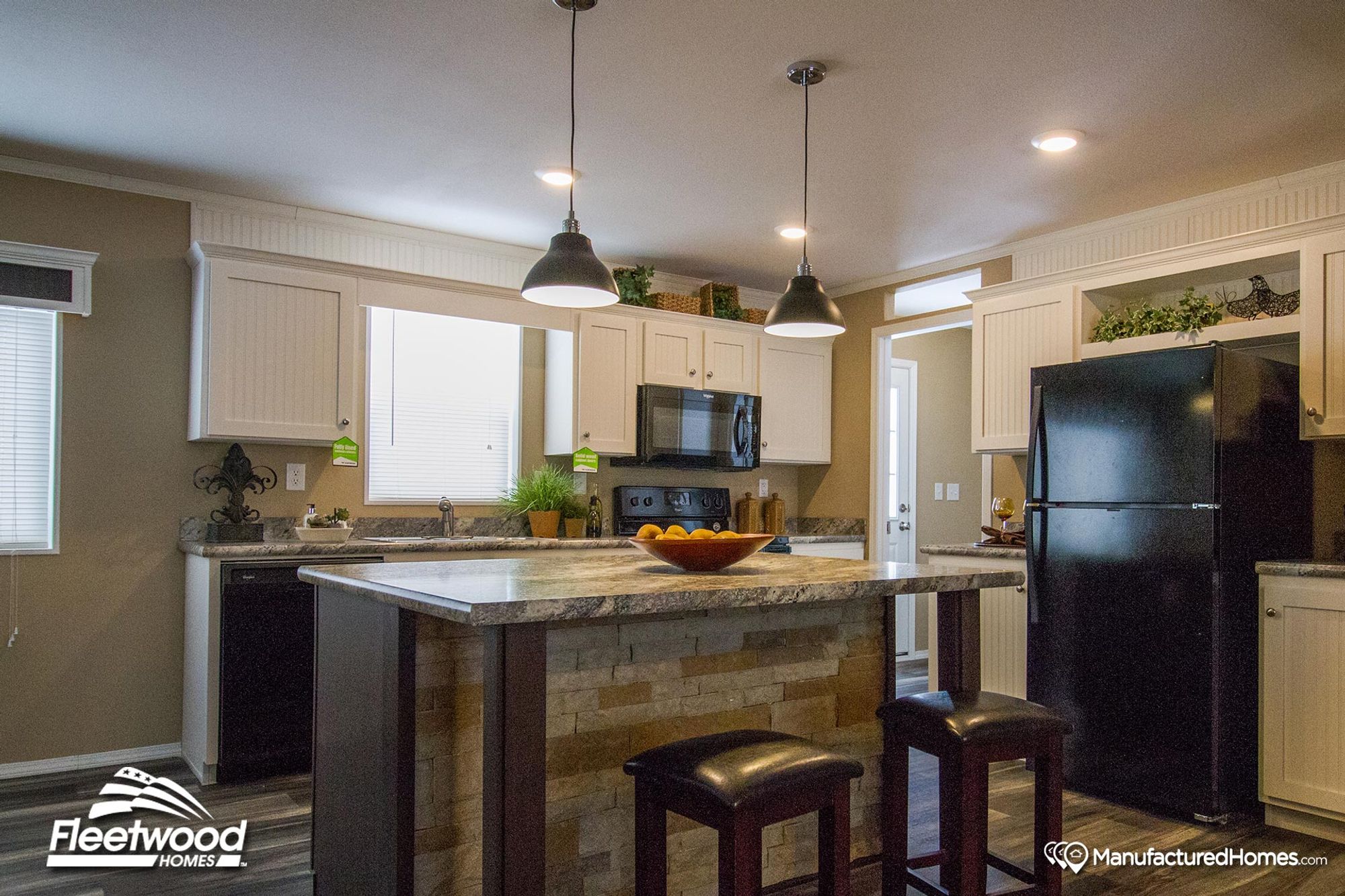 Modern kitchen with a stone-accented island, two pendant lights, white cabinetry, black appliances, and decorative greenery above the cabinets for a cozy touch.