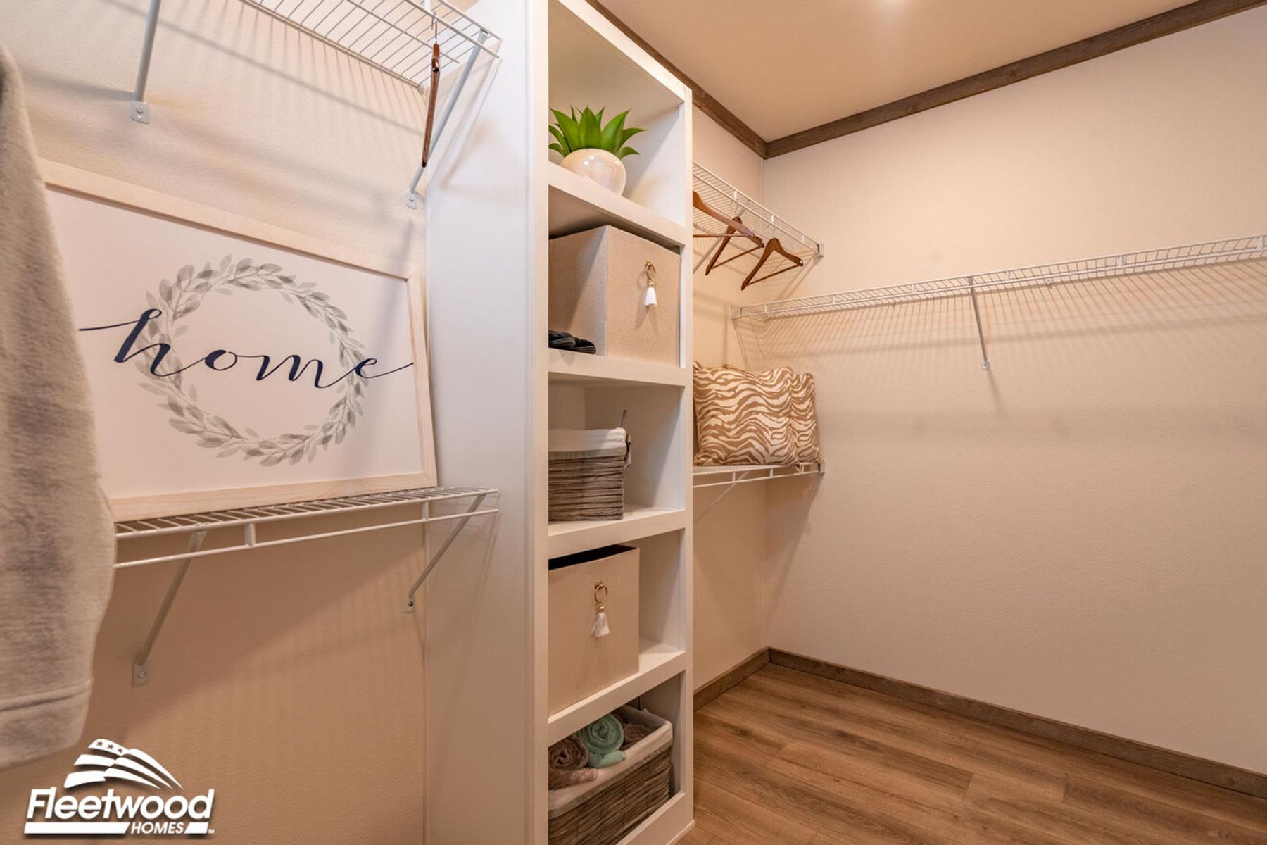 Walk-in closet with built-in shelving, wire racks for hanging clothes, and wood-style flooring, decorated with storage bins and a framed sign.