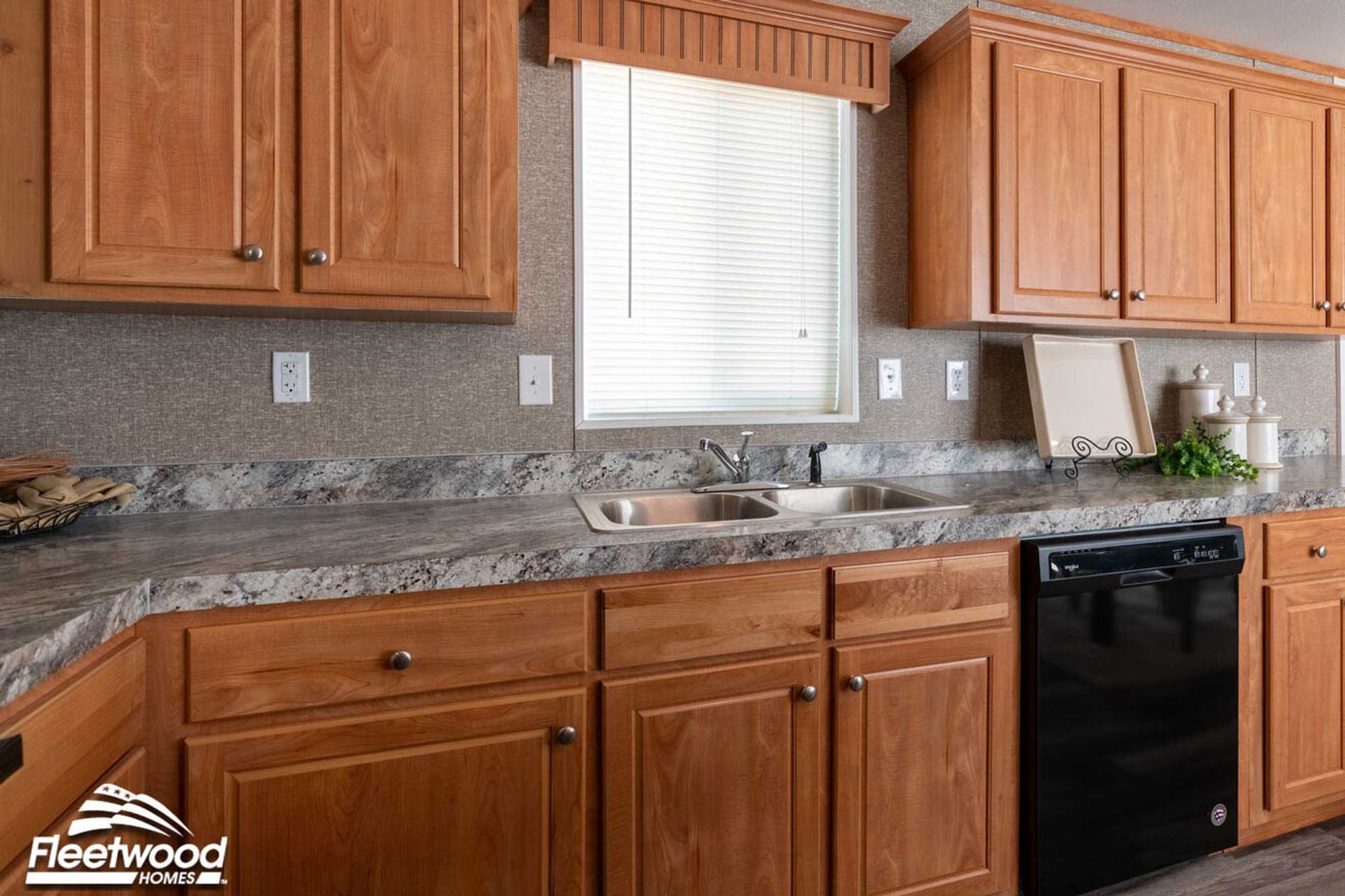 Kitchen with wood cabinets, marble-look countertops, and a double sink beneath a window.