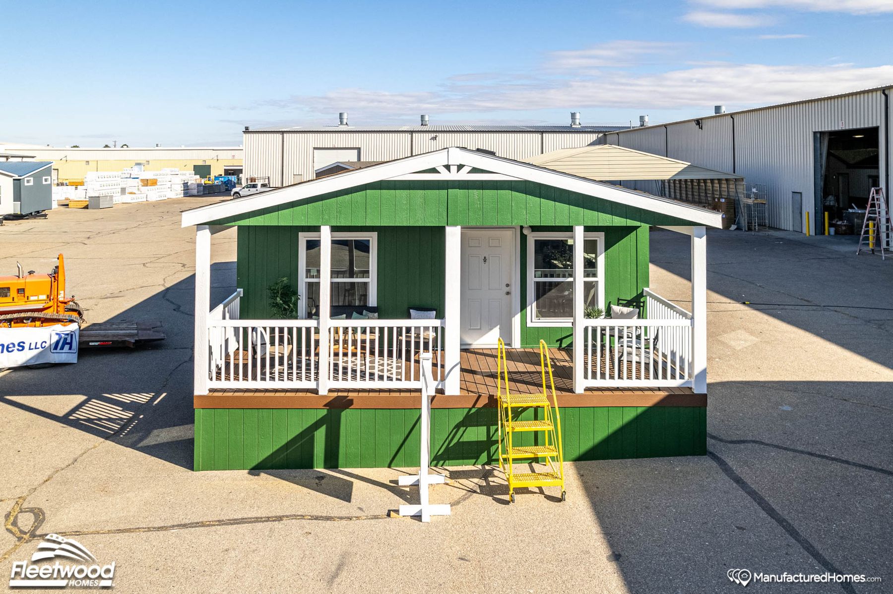 Covered front porch with green siding, outdoor seating, a small table, rug, and potted plant. White front door and railing, with neighboring homes visible in the background.