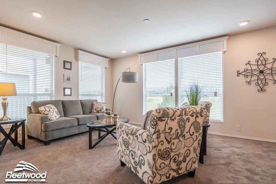 Open living space with patterned armchairs, glass coffee table, and view into a modern kitchen with bar seating and dining area.