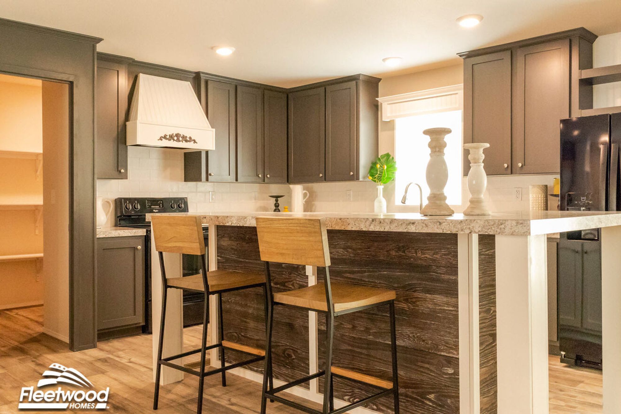 Warm kitchen with granite-style countertops, dark cabinetry, white range hood, black appliances, and a breakfast bar with white candle decor.