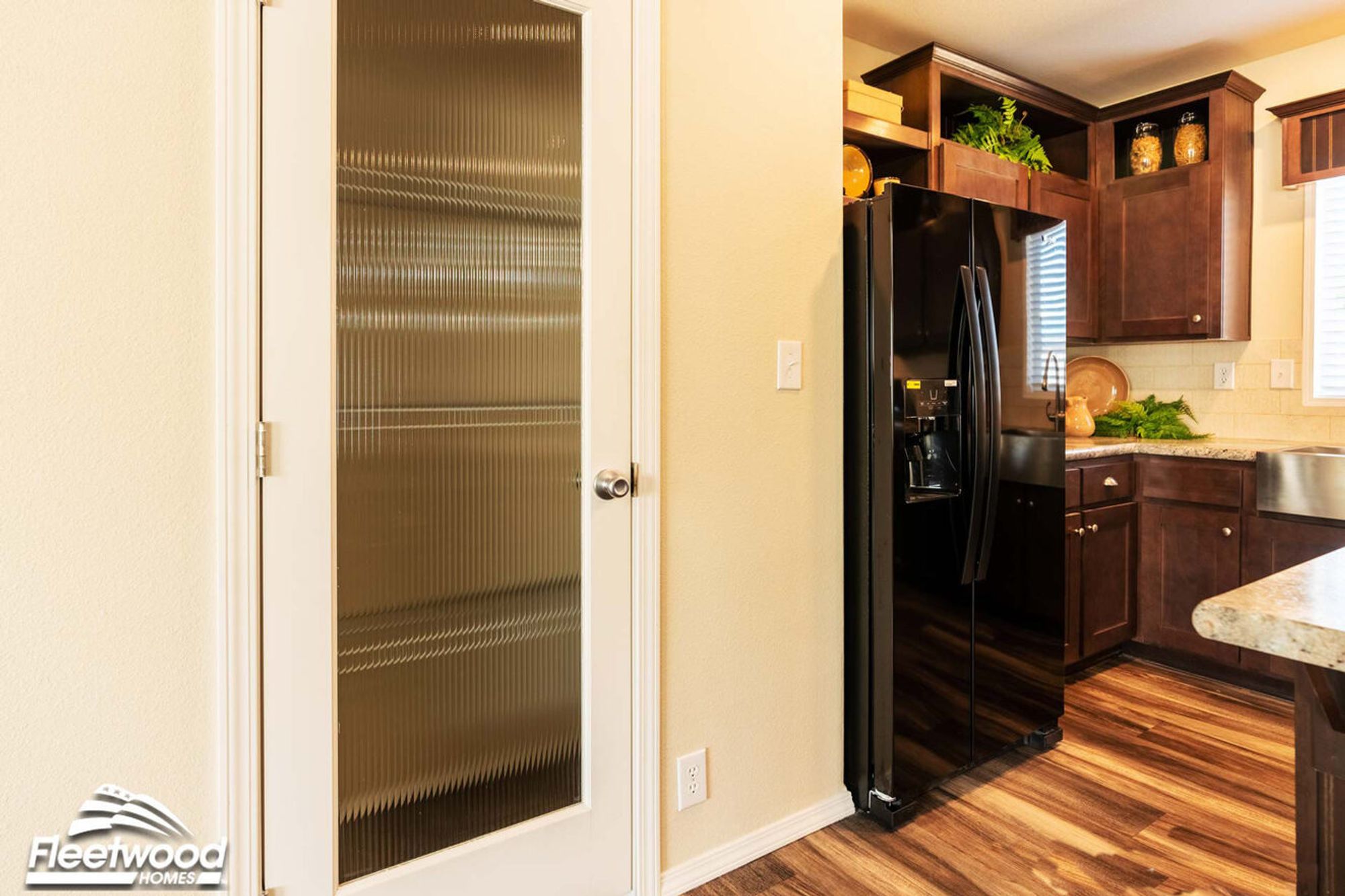 Kitchen corner with dark wood cabinets, black refrigerator, granite countertops, and a frosted glass pantry door.