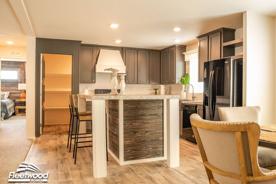Warm kitchen with granite-style countertops, dark cabinetry, white range hood, black appliances, and a breakfast bar with white candle decor.
