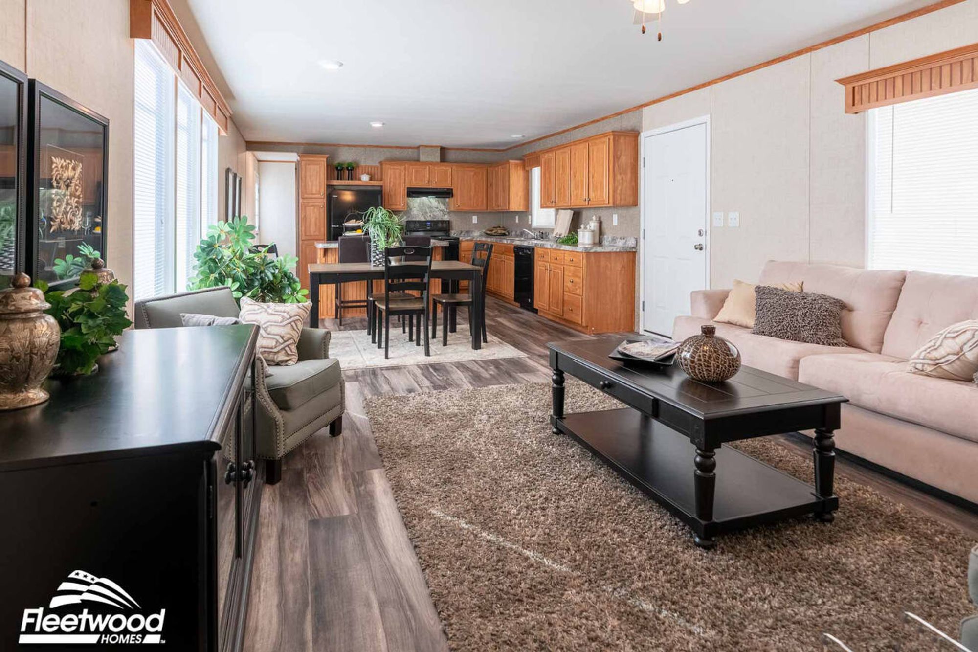 Cozy living room with a beige sofa, two gray armchairs, a dark wood coffee table, and wall art accents under a ceiling fan.