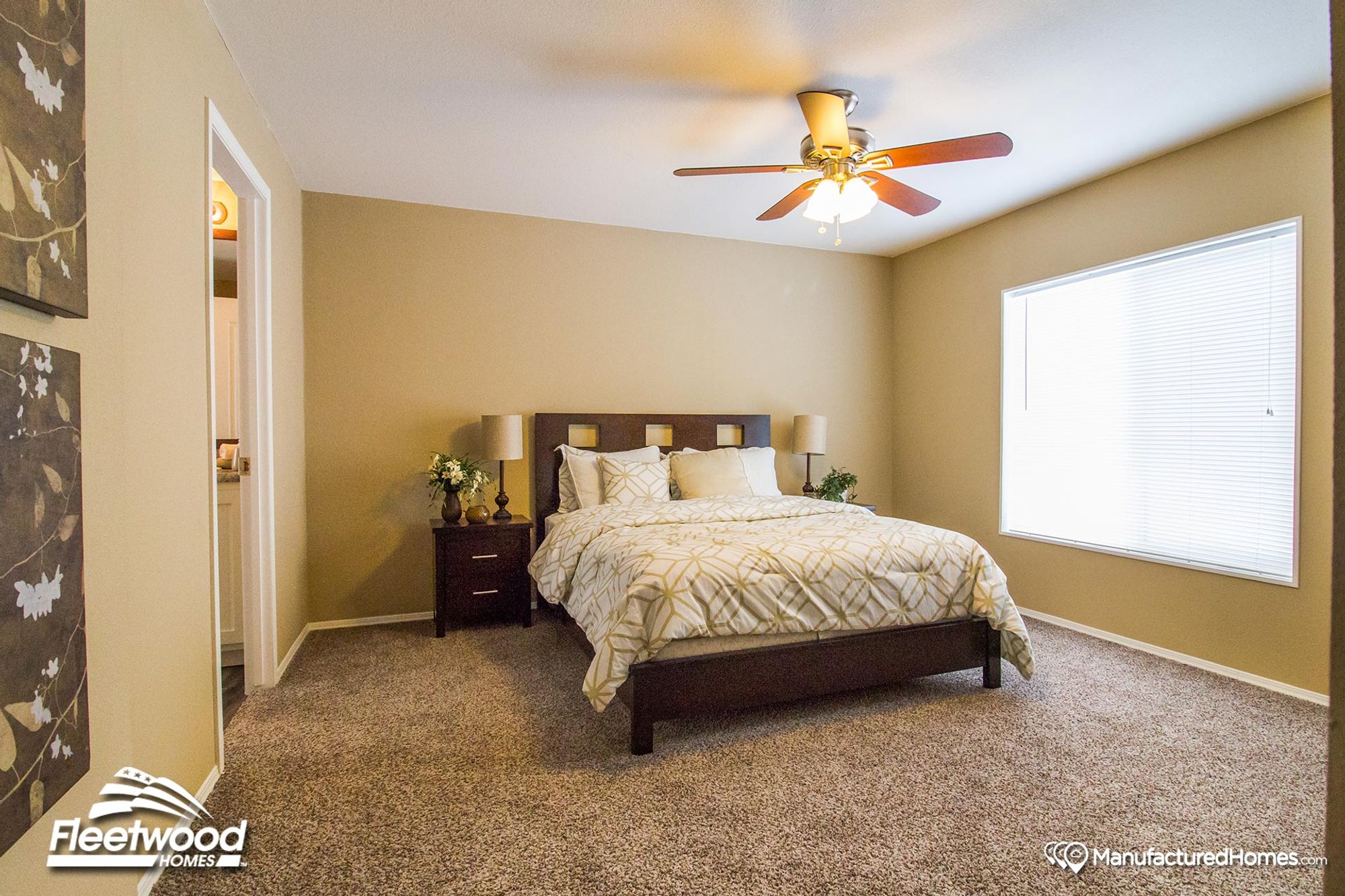 Warm-toned bedroom with a dark wood bed frame, patterned bedding, matching nightstands, and a ceiling fan with light, illuminated by natural light from a large window.