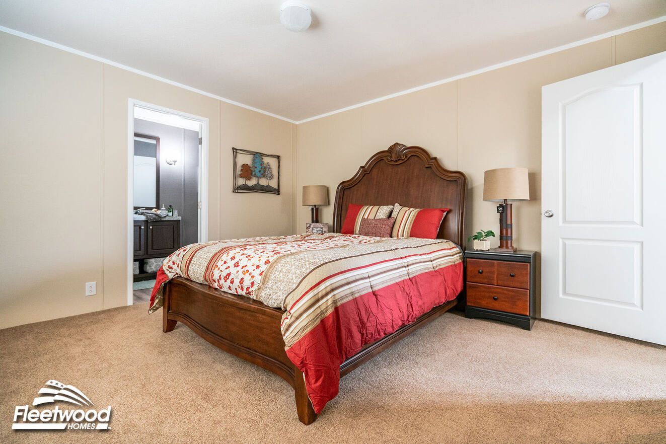 Bedroom with beige walls, carpet flooring, a bed with striped red bedding, and a doorway leading to a bathroom.