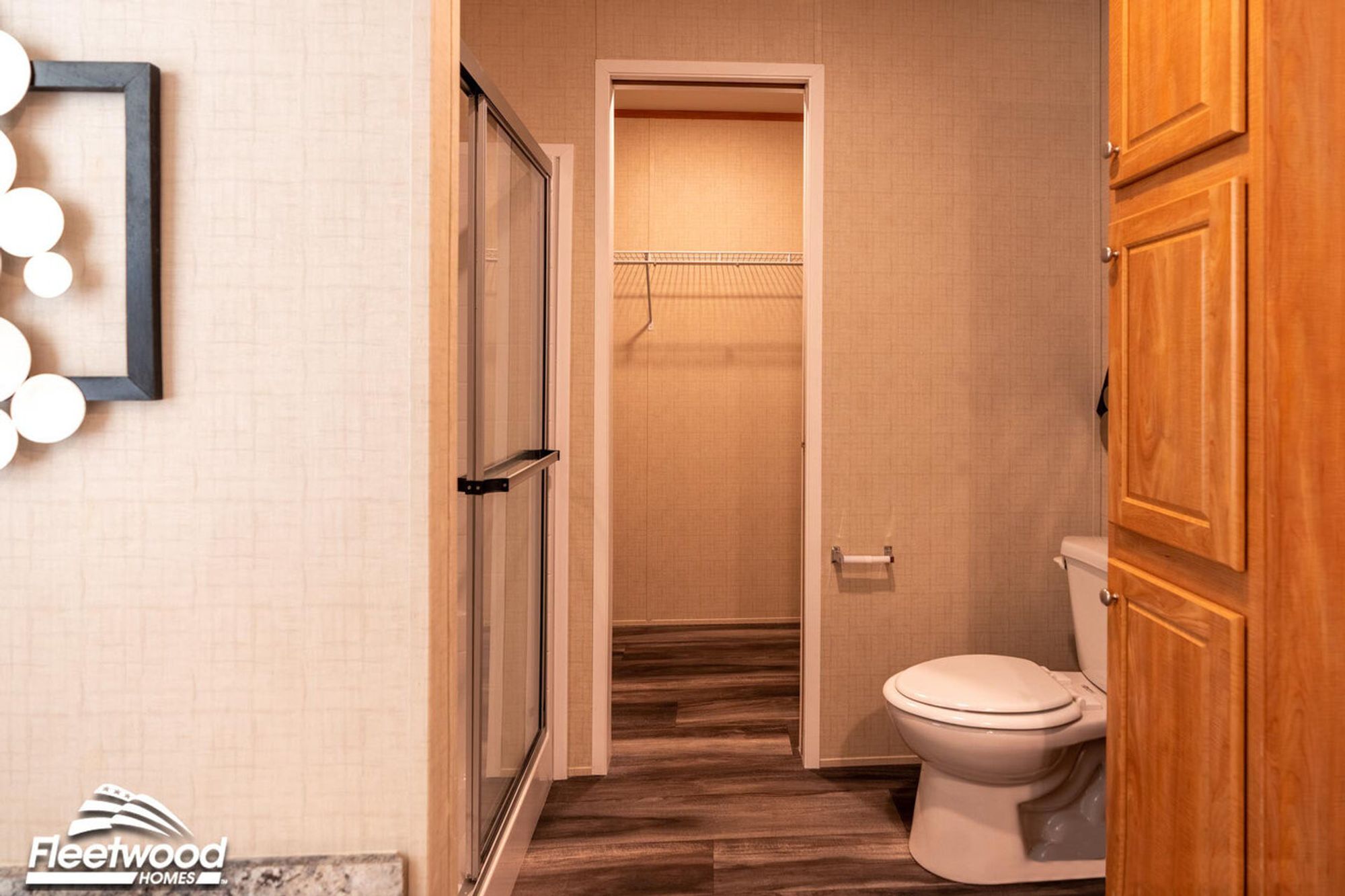 Bathroom with a glass-enclosed shower, toilet, wood cabinetry, and a doorway leading into a walk-in closet with wire shelving.