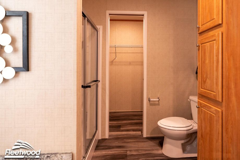 Bathroom with a glass-enclosed shower, toilet, wood cabinetry, and a doorway leading into a walk-in closet with wire shelving.