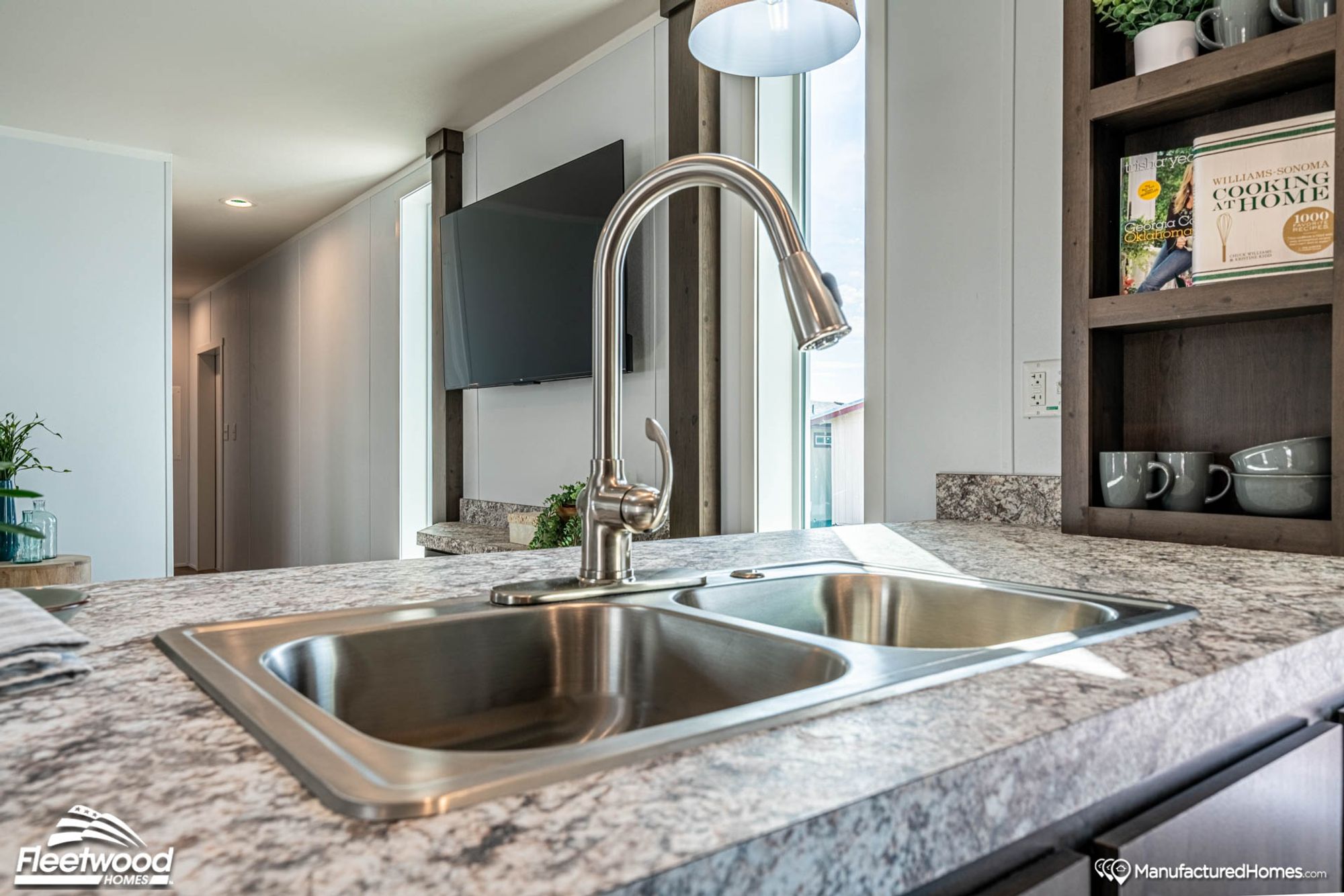 Modern kitchen island with a double-basin stainless steel sink and high-arc pull-down faucet, set in marbled countertops near open shelving and a wall-mounted TV.