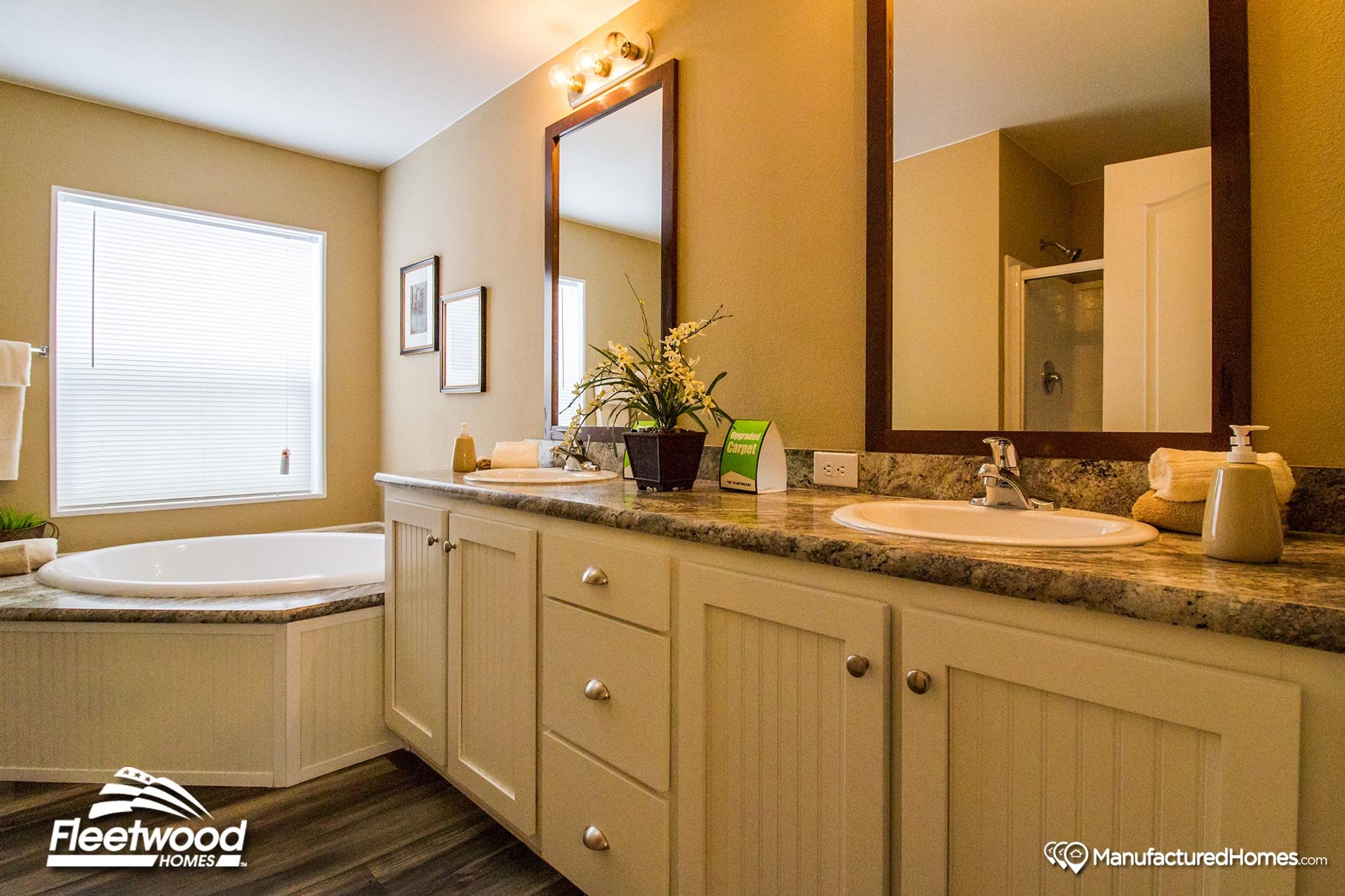 Inviting bathroom with a large corner soaking tub, dual-sink vanity with beadboard cabinets, granite countertops, and two framed mirrors under warm lighting.