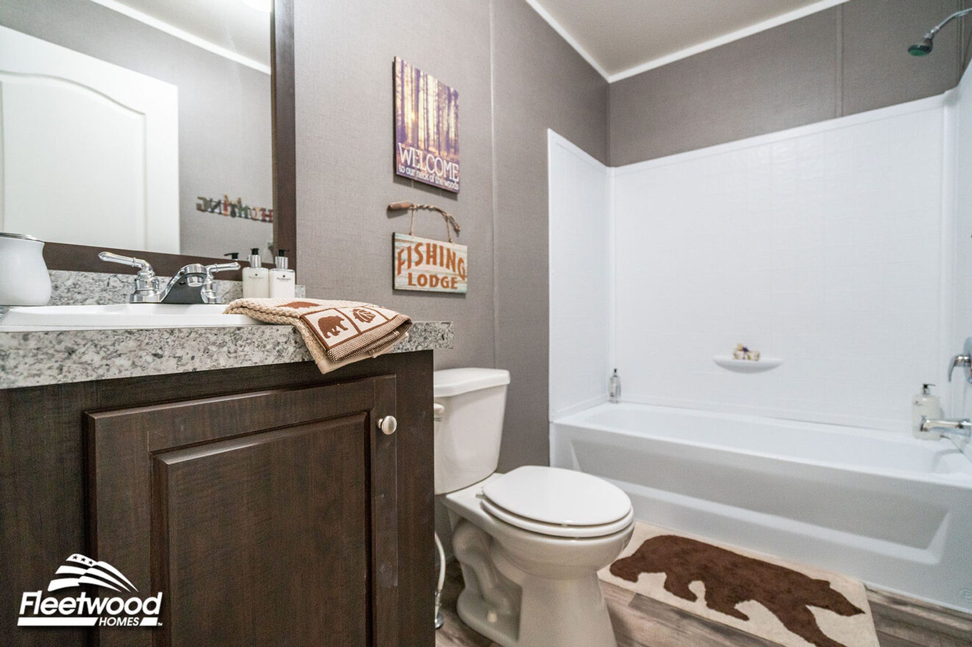 Bathroom with granite-style vanity, dark wood cabinets, a bathtub-shower combo, and rustic lodge-themed decor.