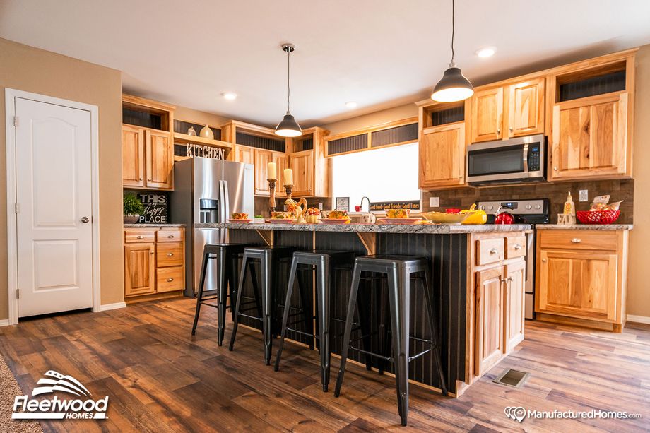 Large kitchen with a mix of light and medium warm wood cabinetry, and pepper-colored style countertops.