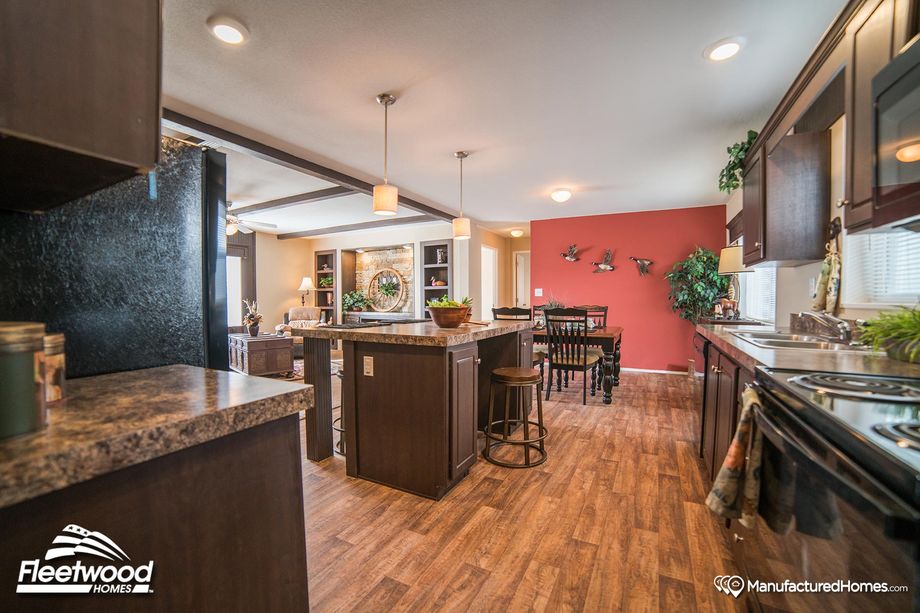 Open concept kitchen, dining room, and living room. The kitchen features brown cabinetry and an island with two stools.