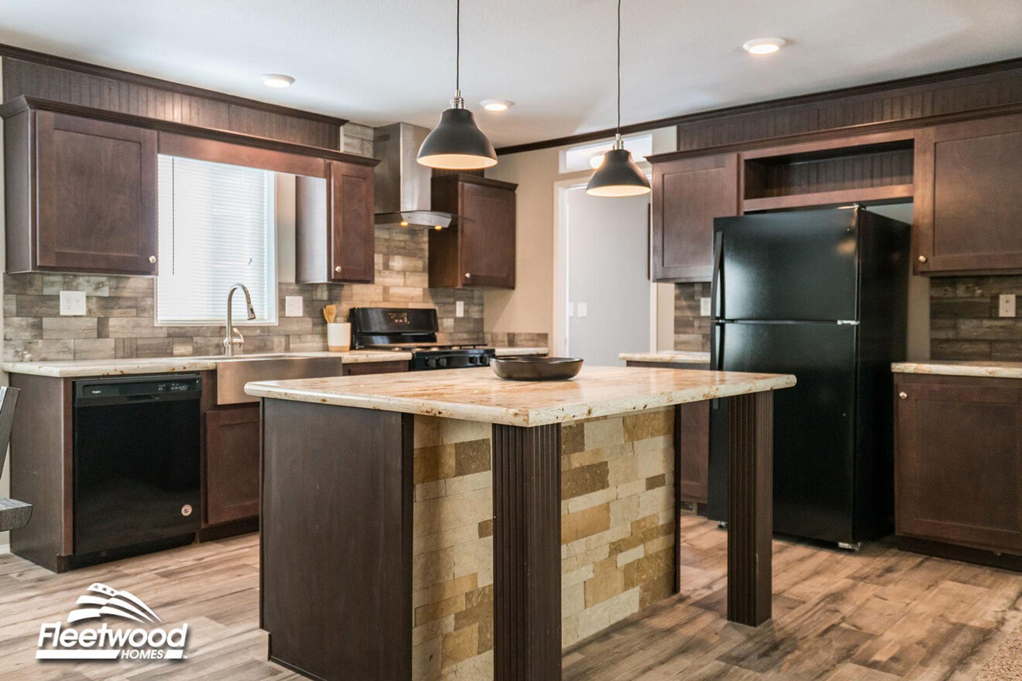 Modern kitchen featuring a central island with a stone facade and granite top, dark cabinetry, black appliances, and pendant lighting above.