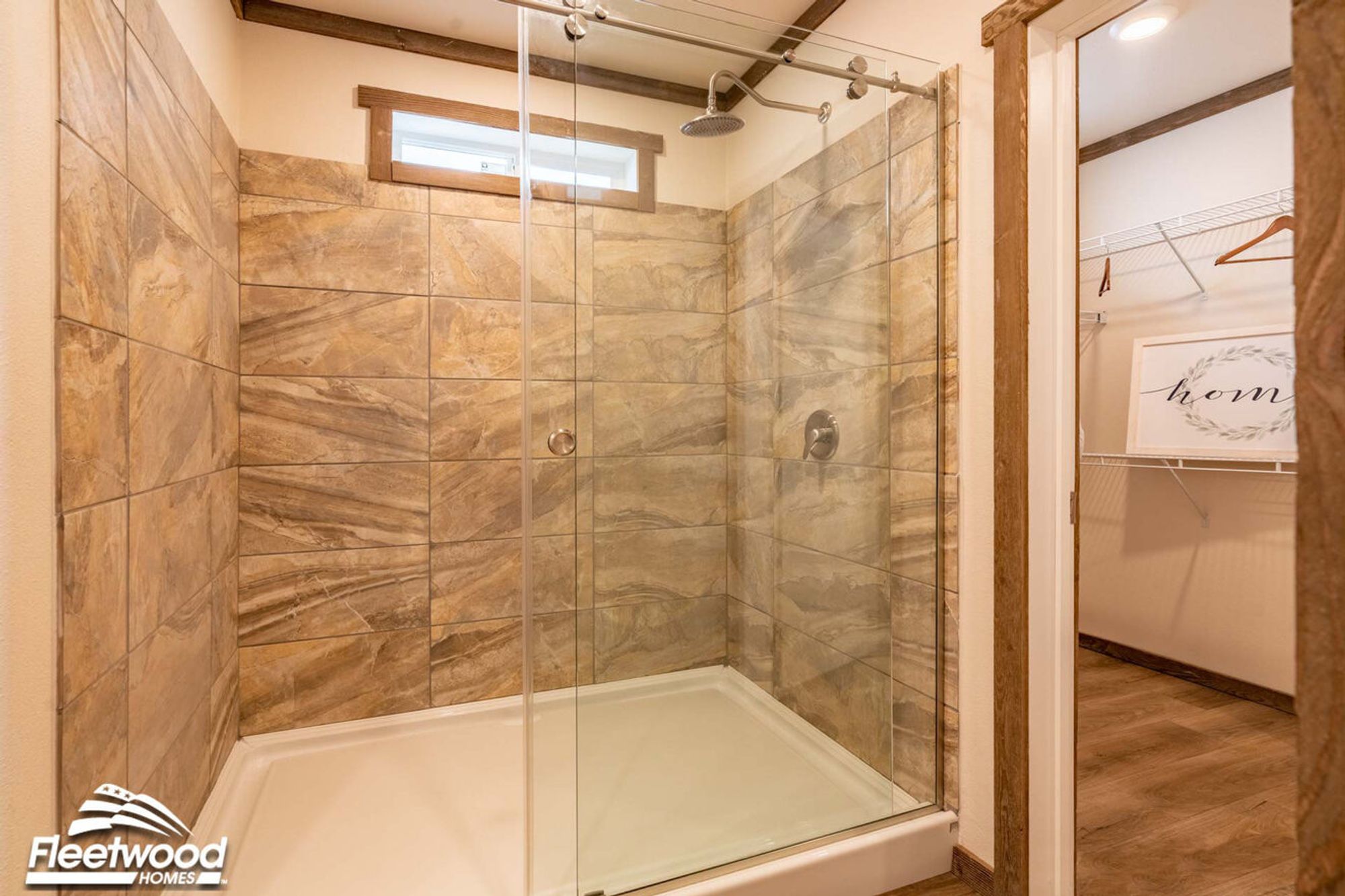 Bathroom with a large walk-in shower featuring sliding glass doors, natural stone-style tile walls, a rainfall showerhead, and an adjacent walk-in closet.