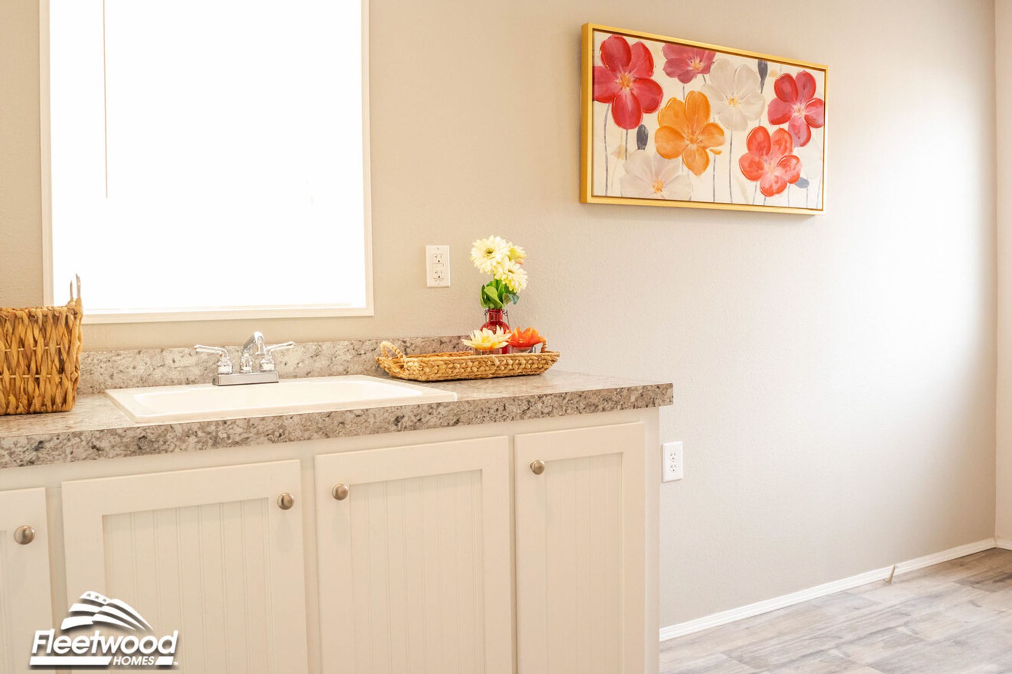 Laundry or utility room with a built-in sink, light granite countertops, white cabinetry, and cheerful floral wall art under a bright window.