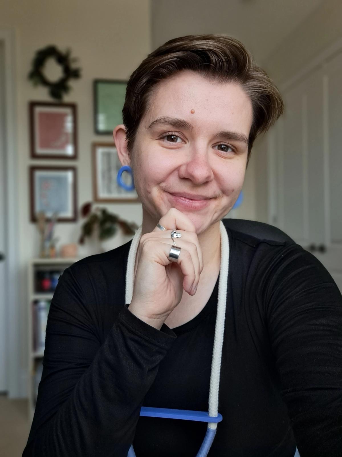 White non-binary person with bright blue accessories and black shirt