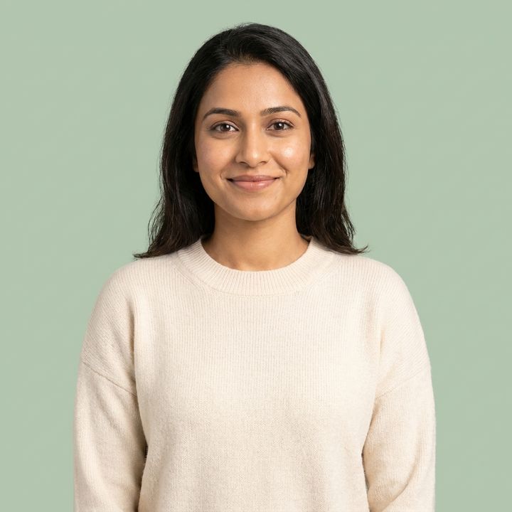 Portrait of a smiling woman in a cream sweater against a soft sage background