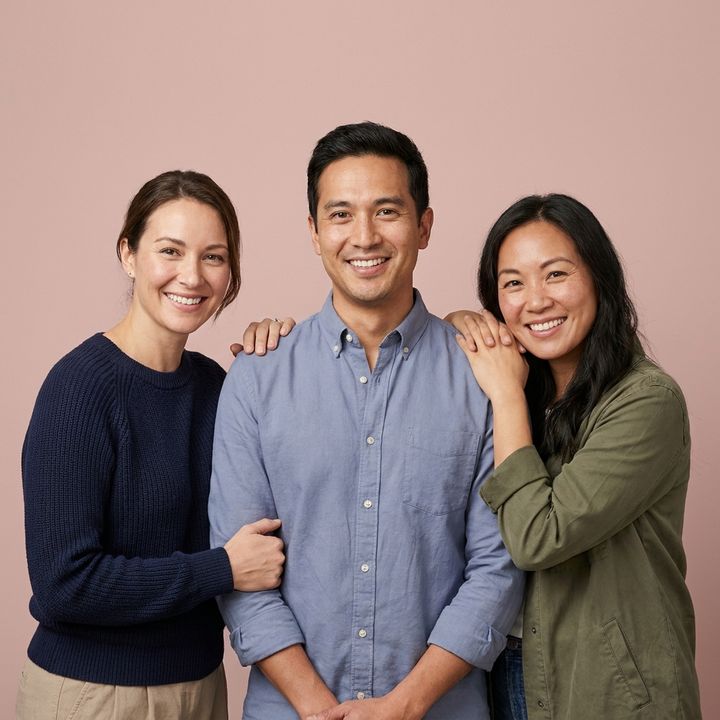 Three smiling adults standing together against a dusty rose background