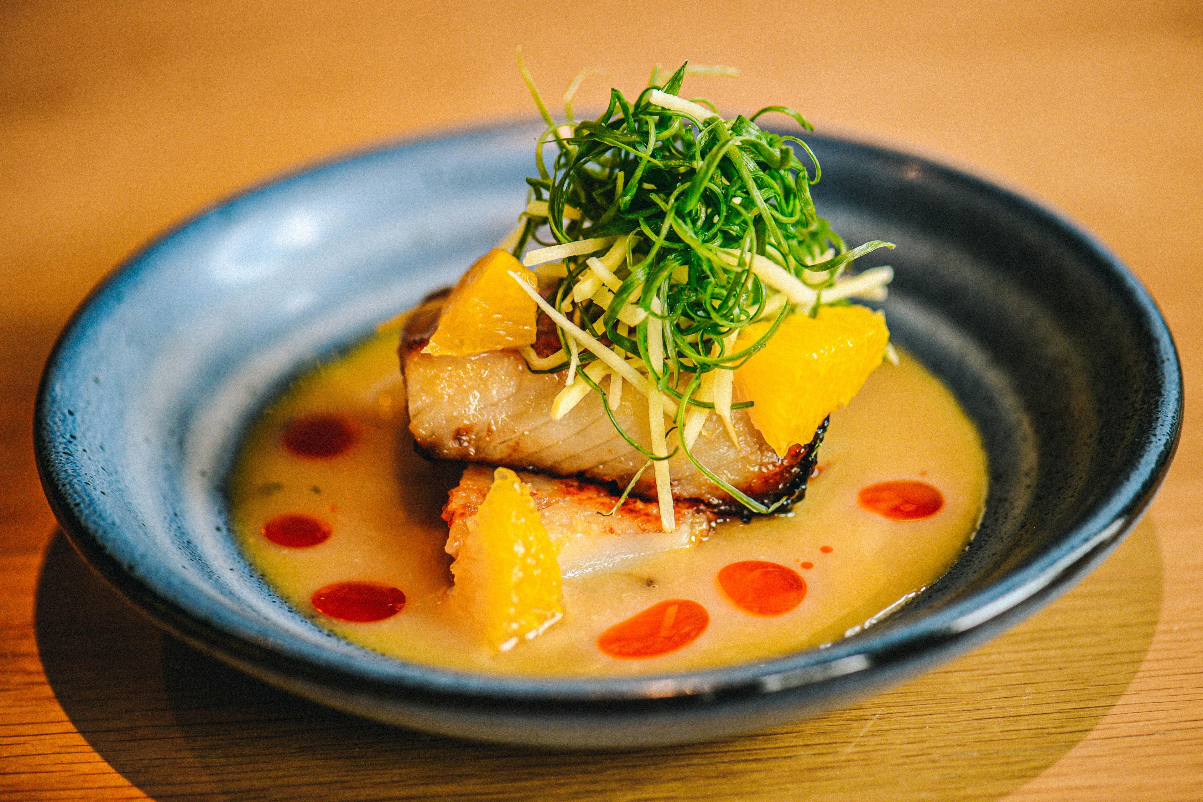 Miso glazed black cod in dish with yuzu miso sauce and garnishes.