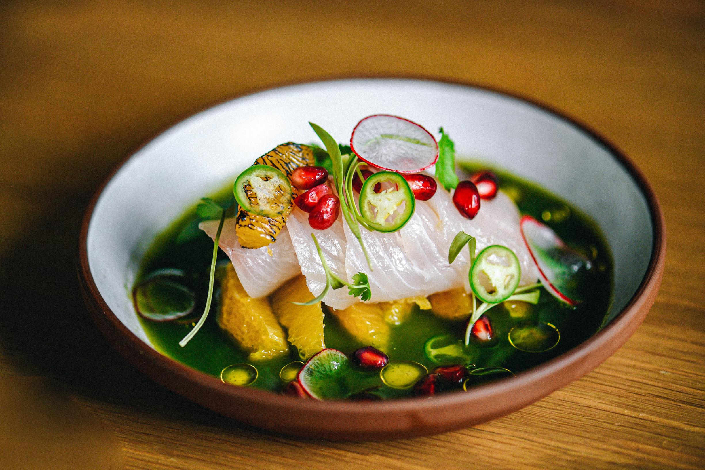 Kanpachi sashimi in dish with cucumber-cilantro aquachile sauce and garnishes.