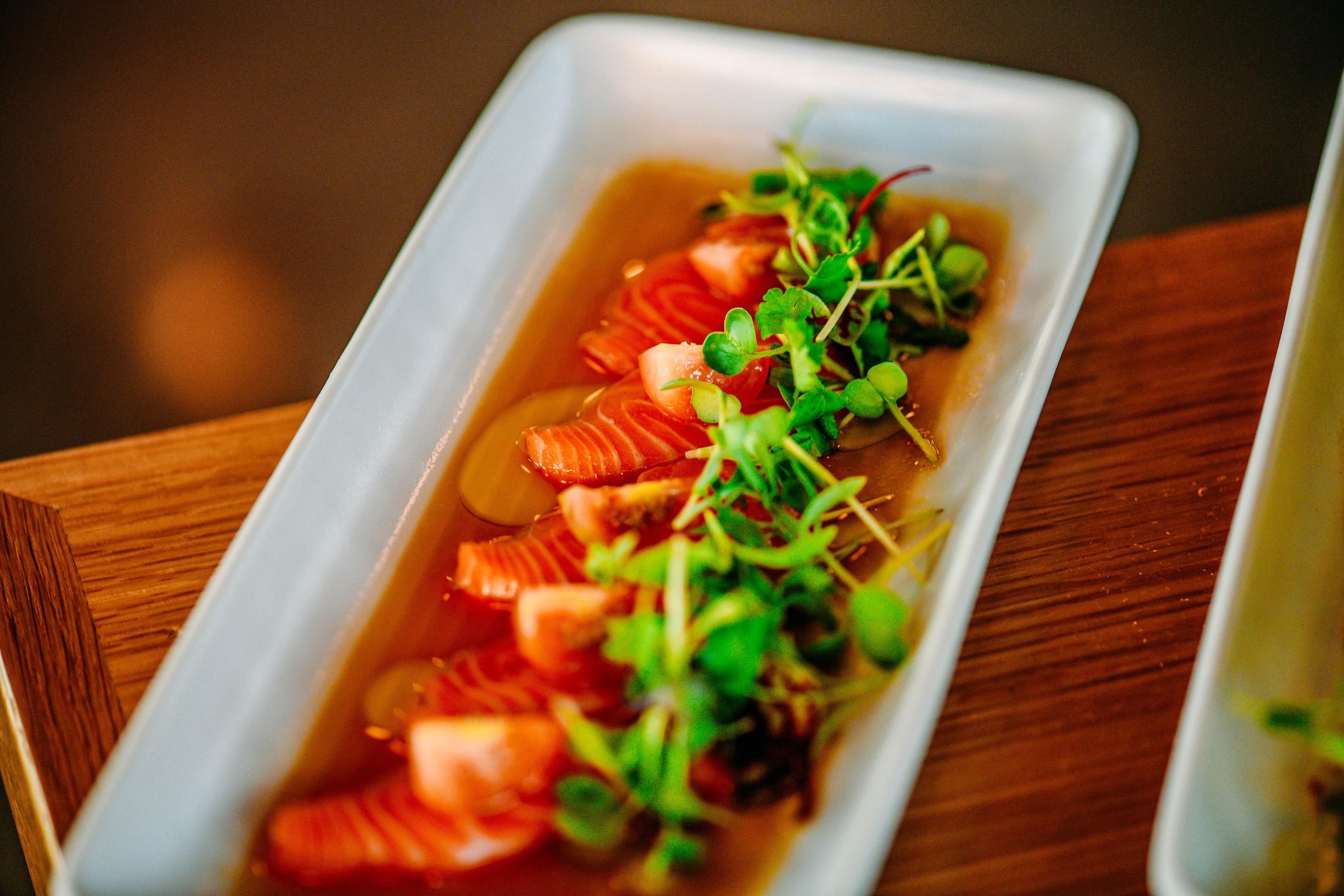 Salmon carpaccio in a dish with a microgreen garnish.