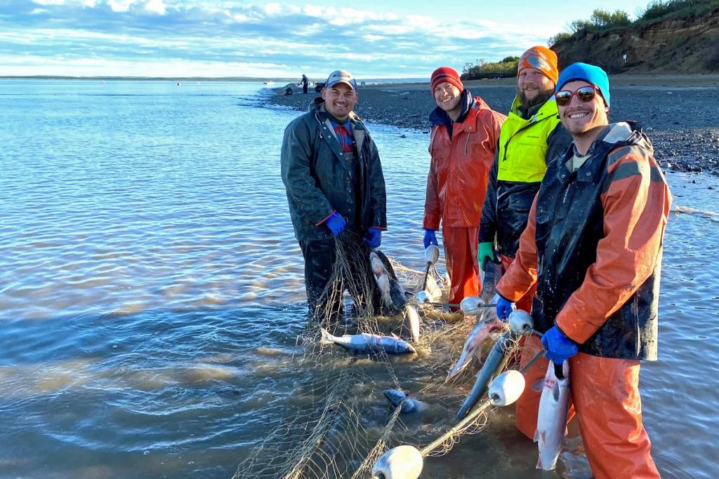 Workers holding a net while they stand in the ocean, just off of a beach.