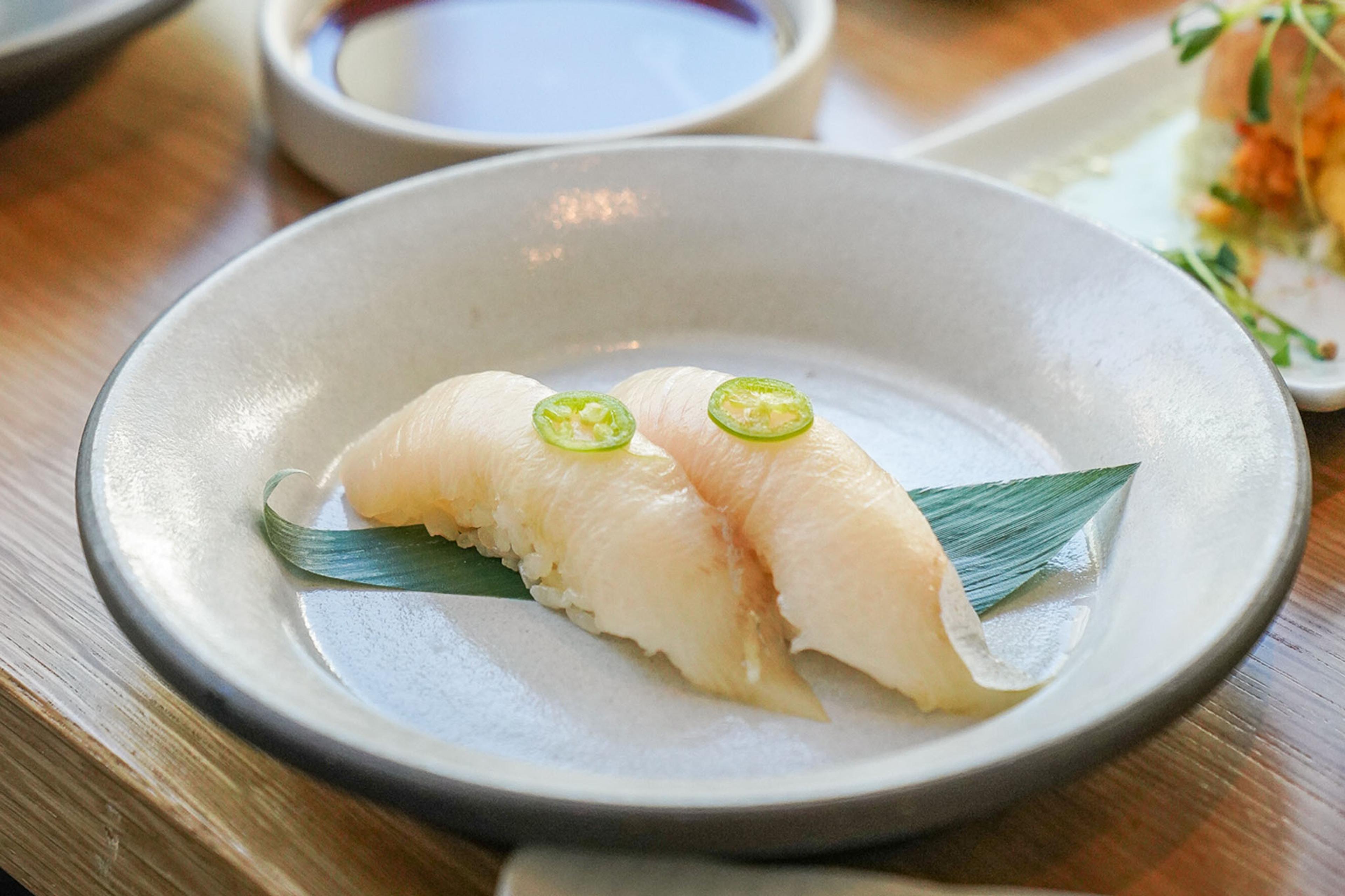 Hamachi nigiri in a dish with a garnish of jalapeno.