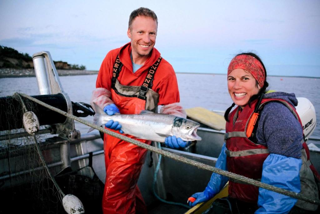 Iliamna Fish Co crew holding up a large fish and grinning.