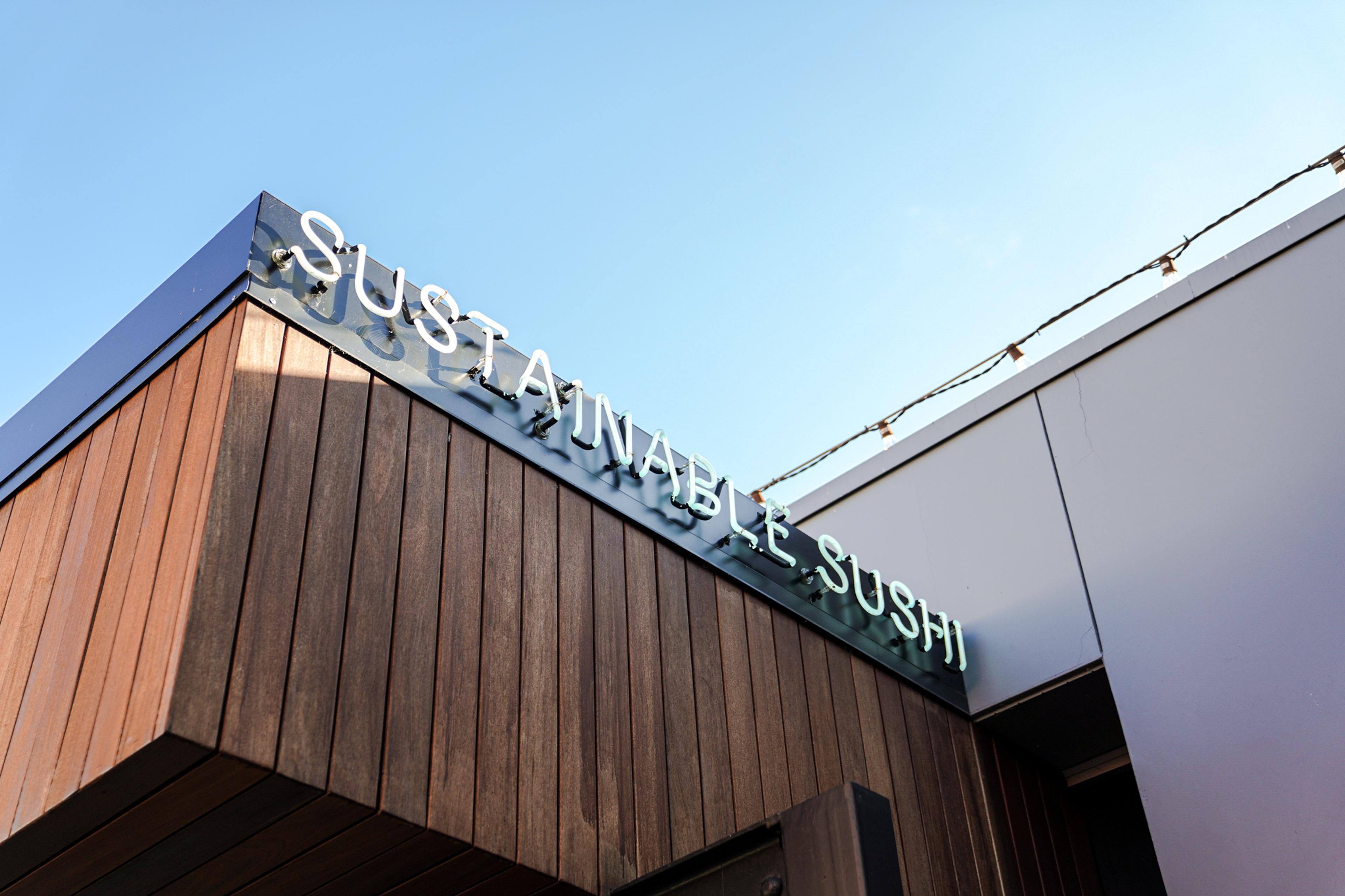 A neon "Sustainable Sushi" sign at the entrance of the University Village Bamboo Sushi restaurant.