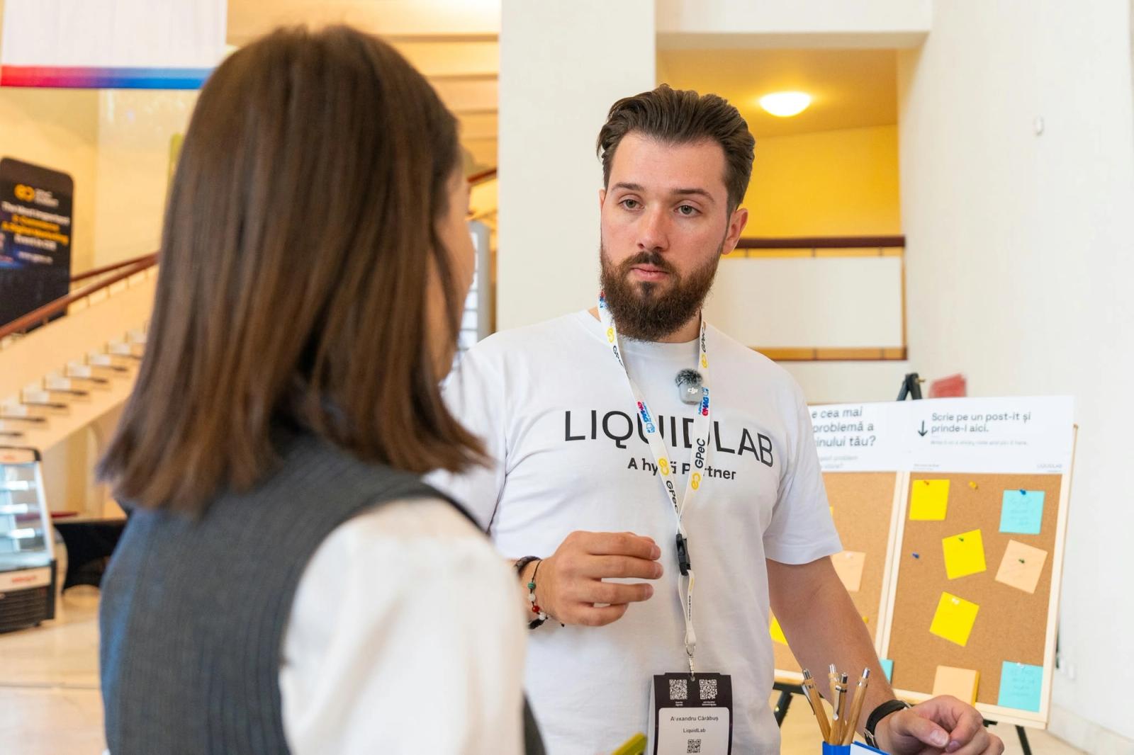 Alexandru-Manuel Carabus of LIQUIDLAB talks with a visitor next to the sticky-note board at GPeC SUMMIT 2026.