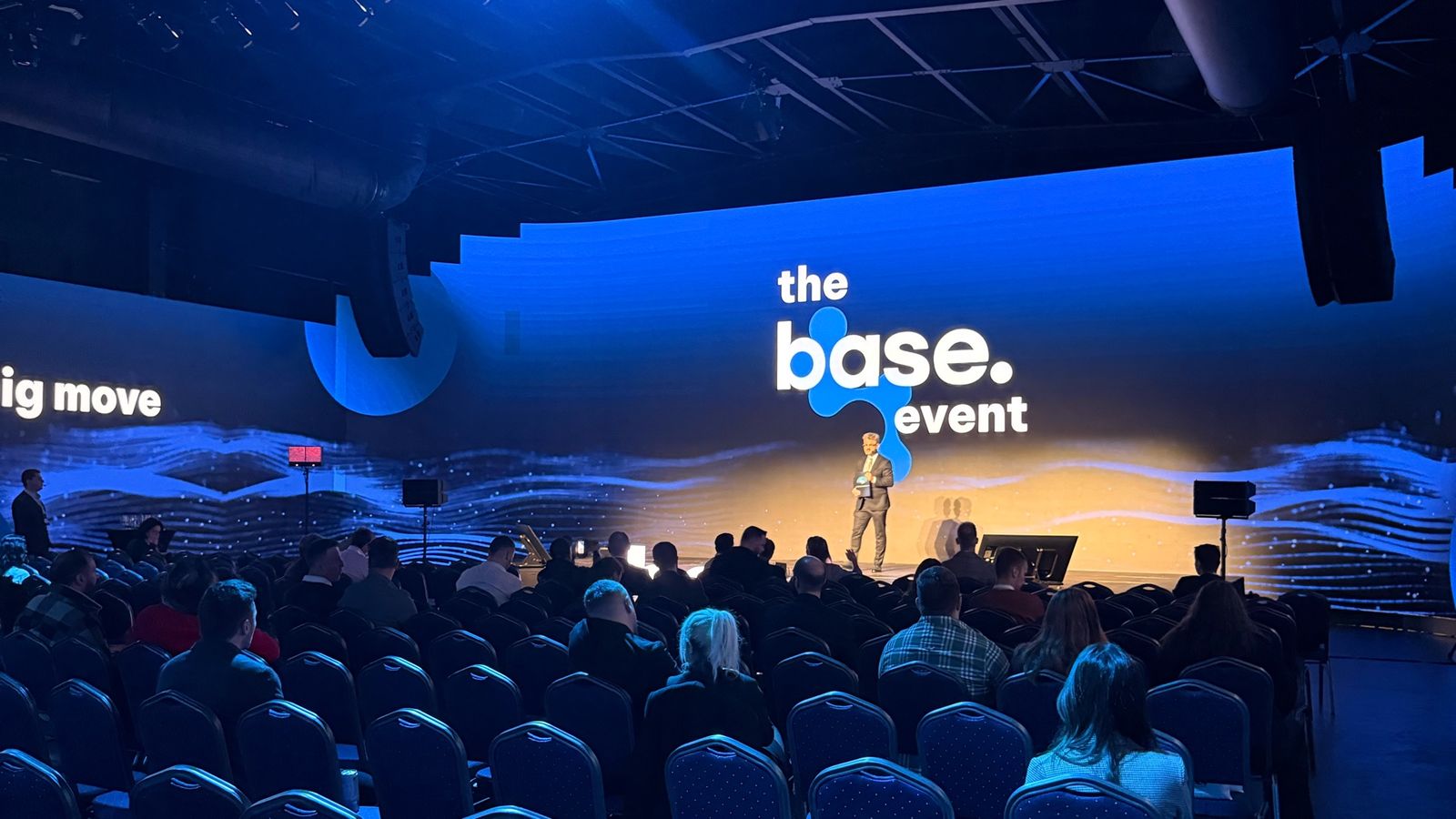 The Base Event 2026 stage at HALO Events Center in Bucharest, with "the base. event" on the screen and the audience in the hall.