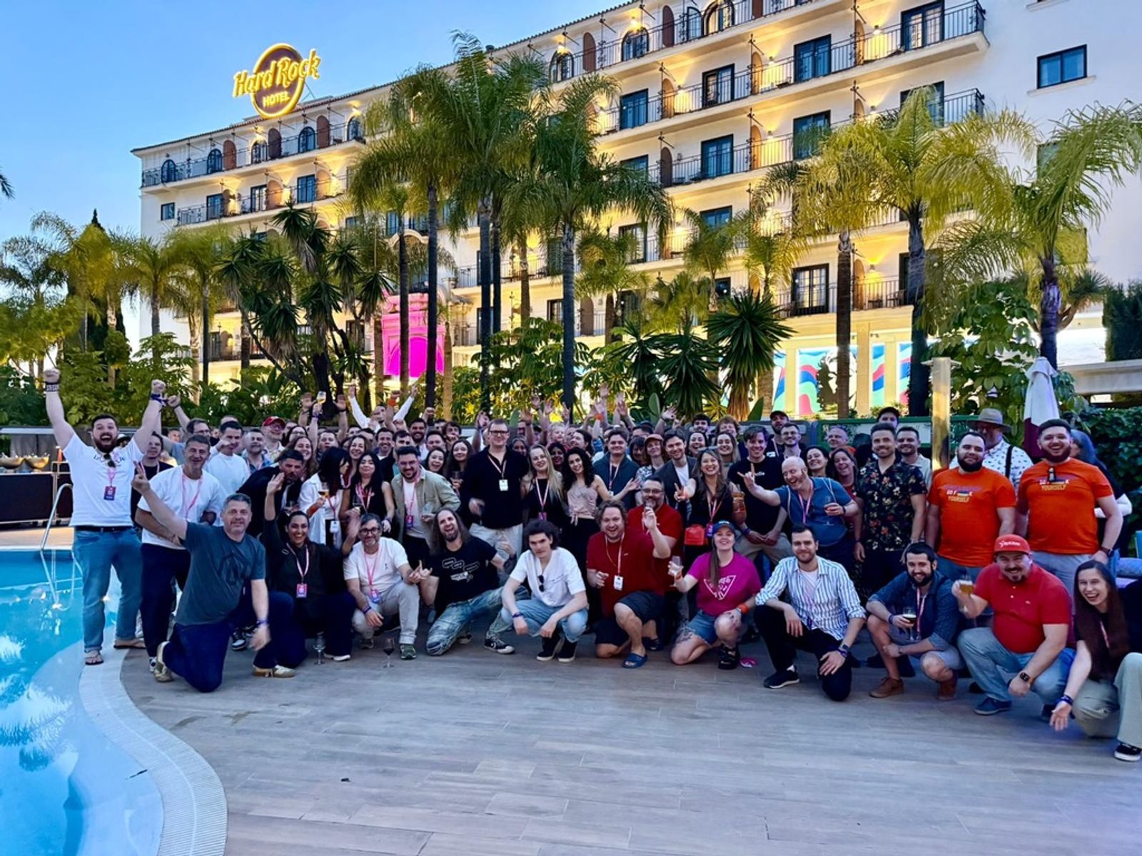 O fotografie de grup cu numeroși dezvoltatori și participanți pozând împreună lângă o piscină la Hard Rock Hotel în timpul evenimentului Hyvä Developer Paradise 2026, surprinzând spiritul de colaborare și comunitate al ecosistemului Magento și Hyvä.